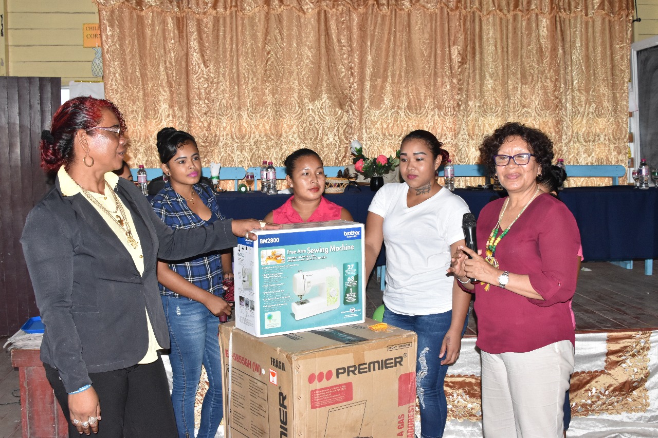 Minister within the Ministry of Indigenous Peoples’ Affairs Valerie Garrido-Lowe (left) handing over the equipment to Chairperson of Canal Bank, Stephanie Miguel and HEYS participants