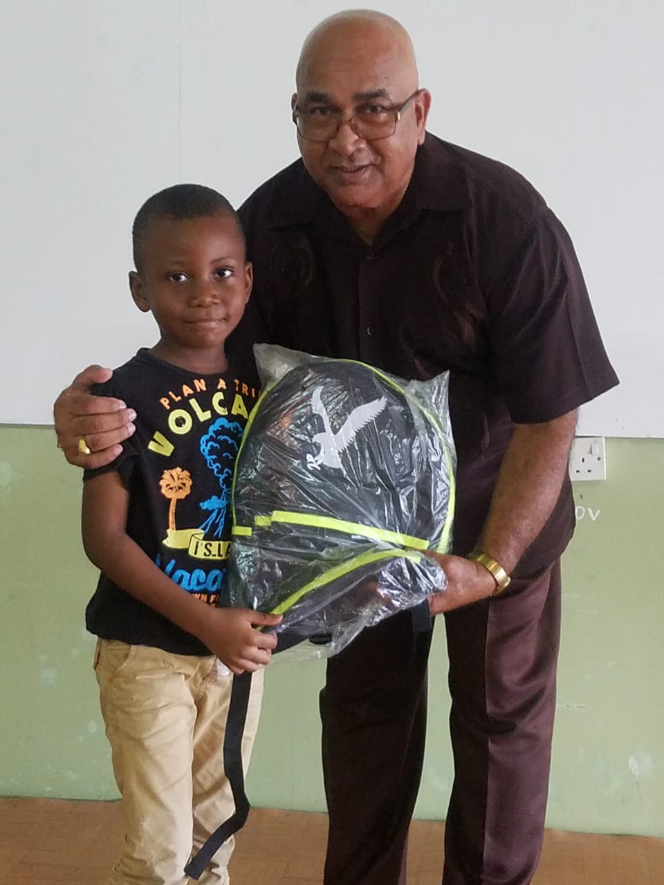 Regional Executive Officer Denis Jaikaran presents a school bag to a student