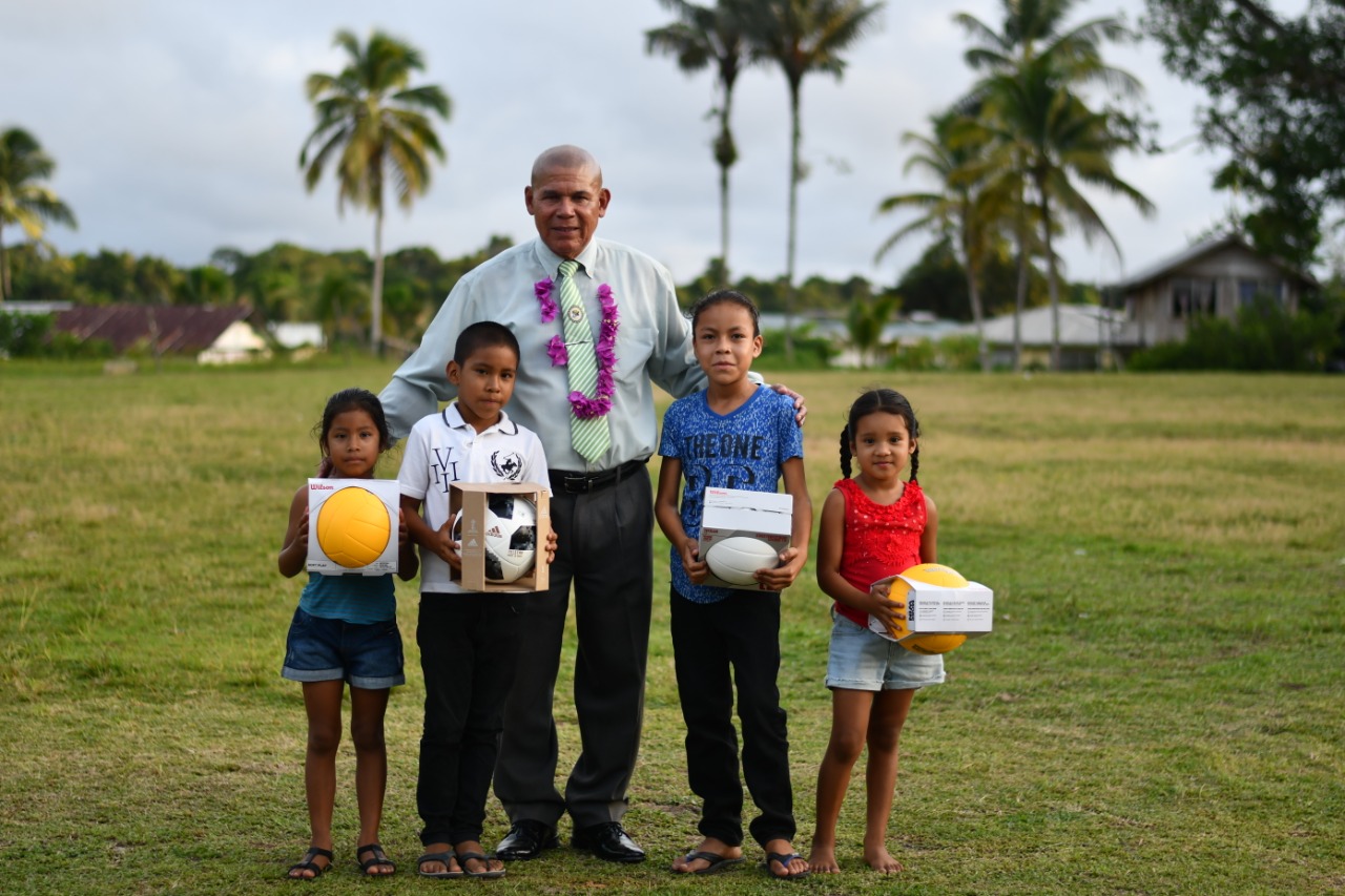Minister of Social Cohesion Hon. Dr. George with some of the children of Tapakuma with some of the volleyballs and footballs presented to the community