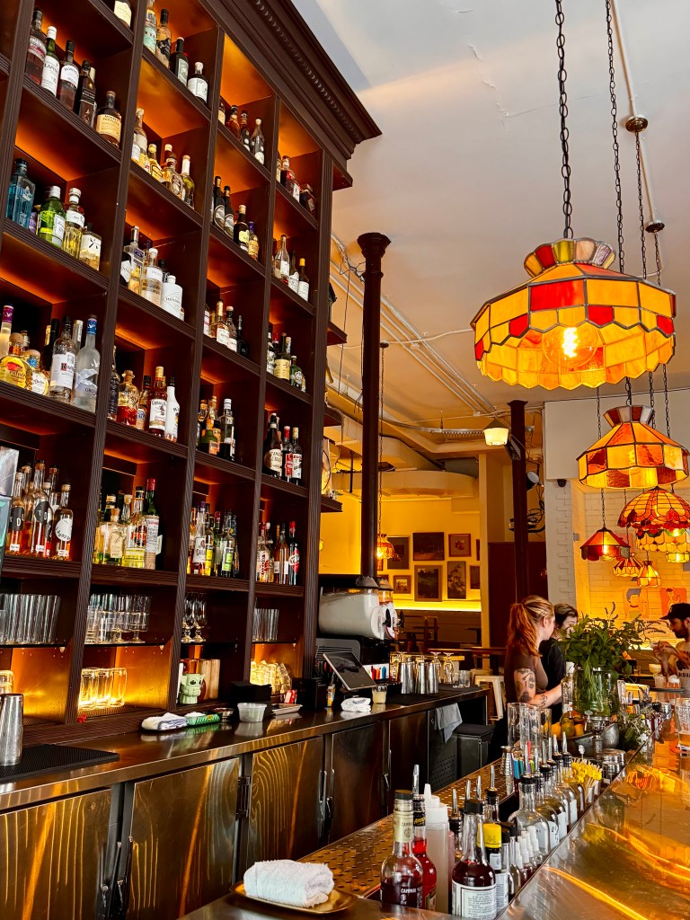 Image of a bar with tall shelves full of bottles and stained glass lampshades