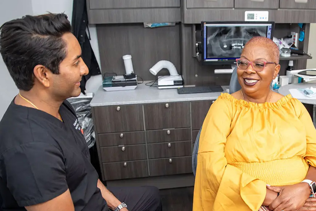 Smiling patient in dental office consulting with dentist, discussing dental implant options in a modern, welcoming environment.
