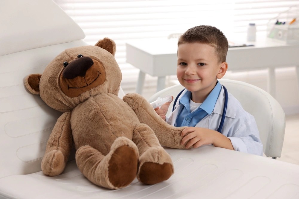 Criança vestido de médico ao lado de urso de pelúcia