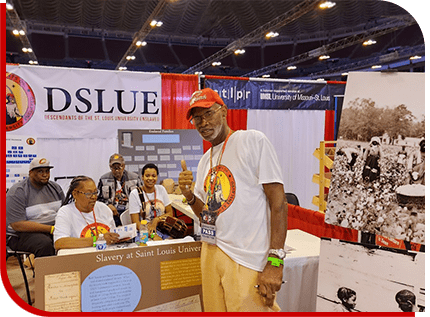 A Man Stands Beside a Table Displaying a Sign That Reads “Dslue.