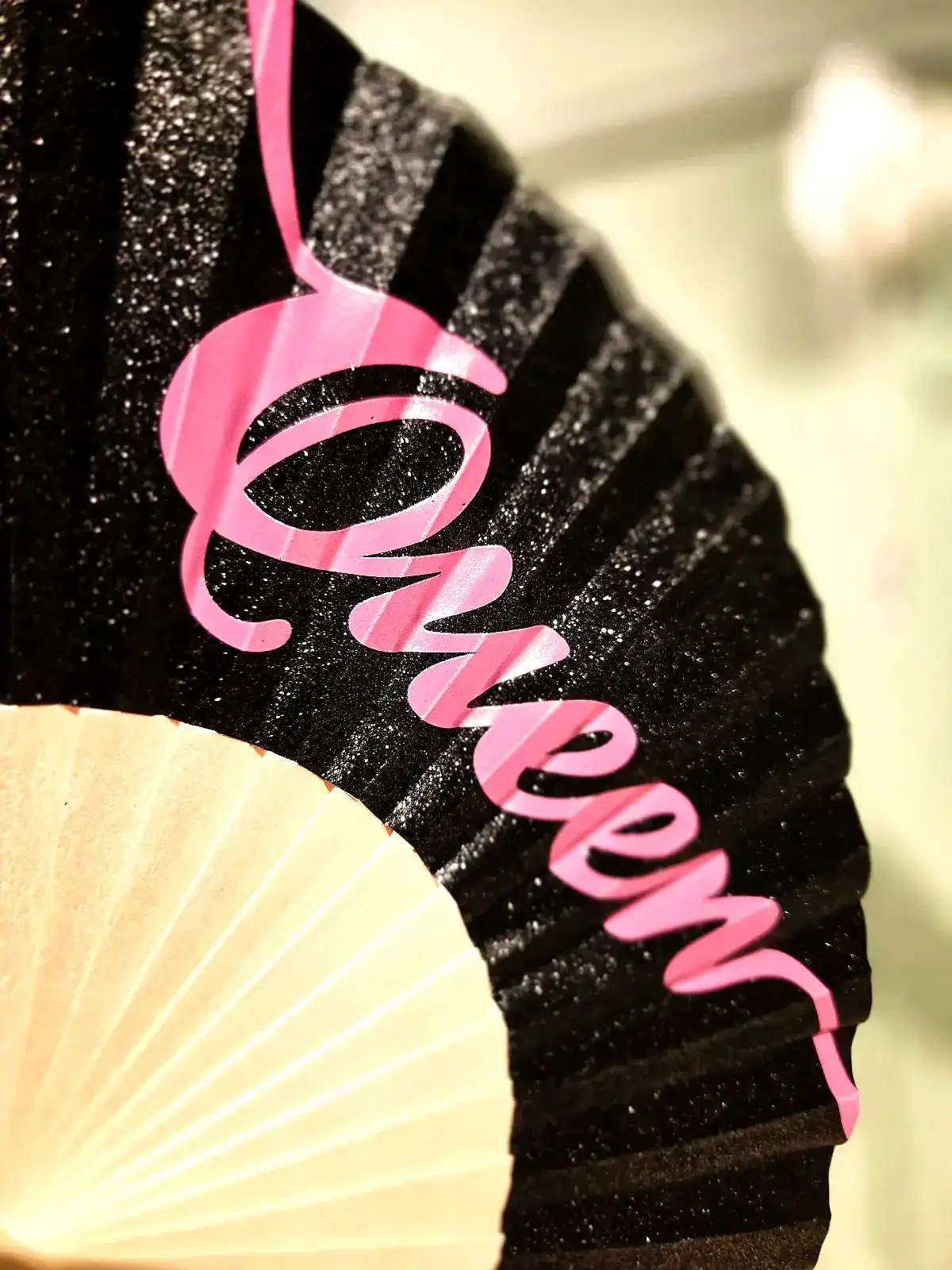 Fan med "Queen" tekst i lyserødt på sort glitterbaggrund, perfekt til fest og festlige anledninger.