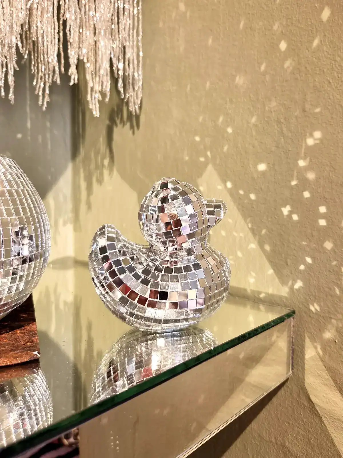 Reflekterende disco duck figur med spejlfliser på glasbord.
