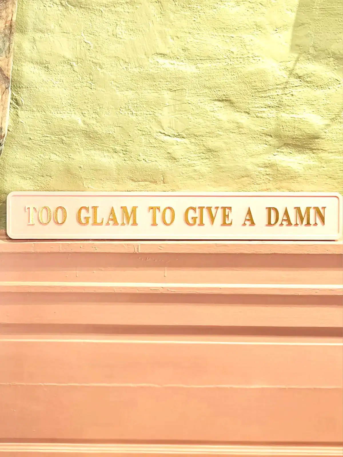 Vægdekoration med citatet '100 GLAM TO GIVE A DAMN' i pastelfarver.
