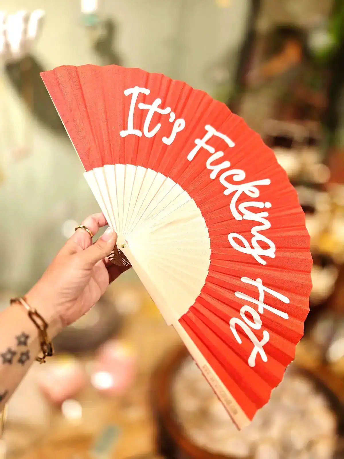 Fan med teksten 'It's Fucking Hot' i rød og hvid farve.