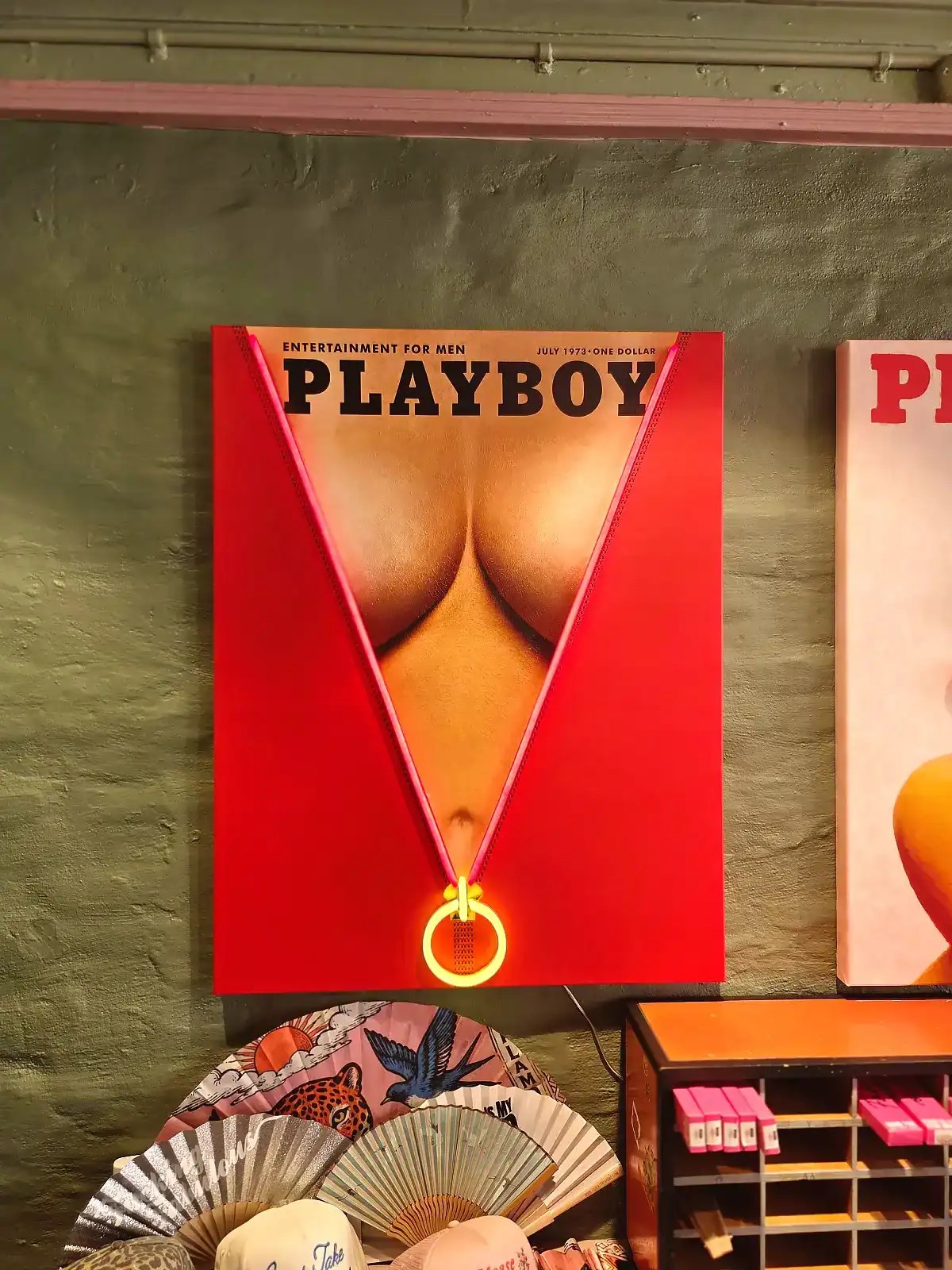 Vægspejl med Playboy-omslag, der viser en kvindes bagdel i en gulddel af en medalje.