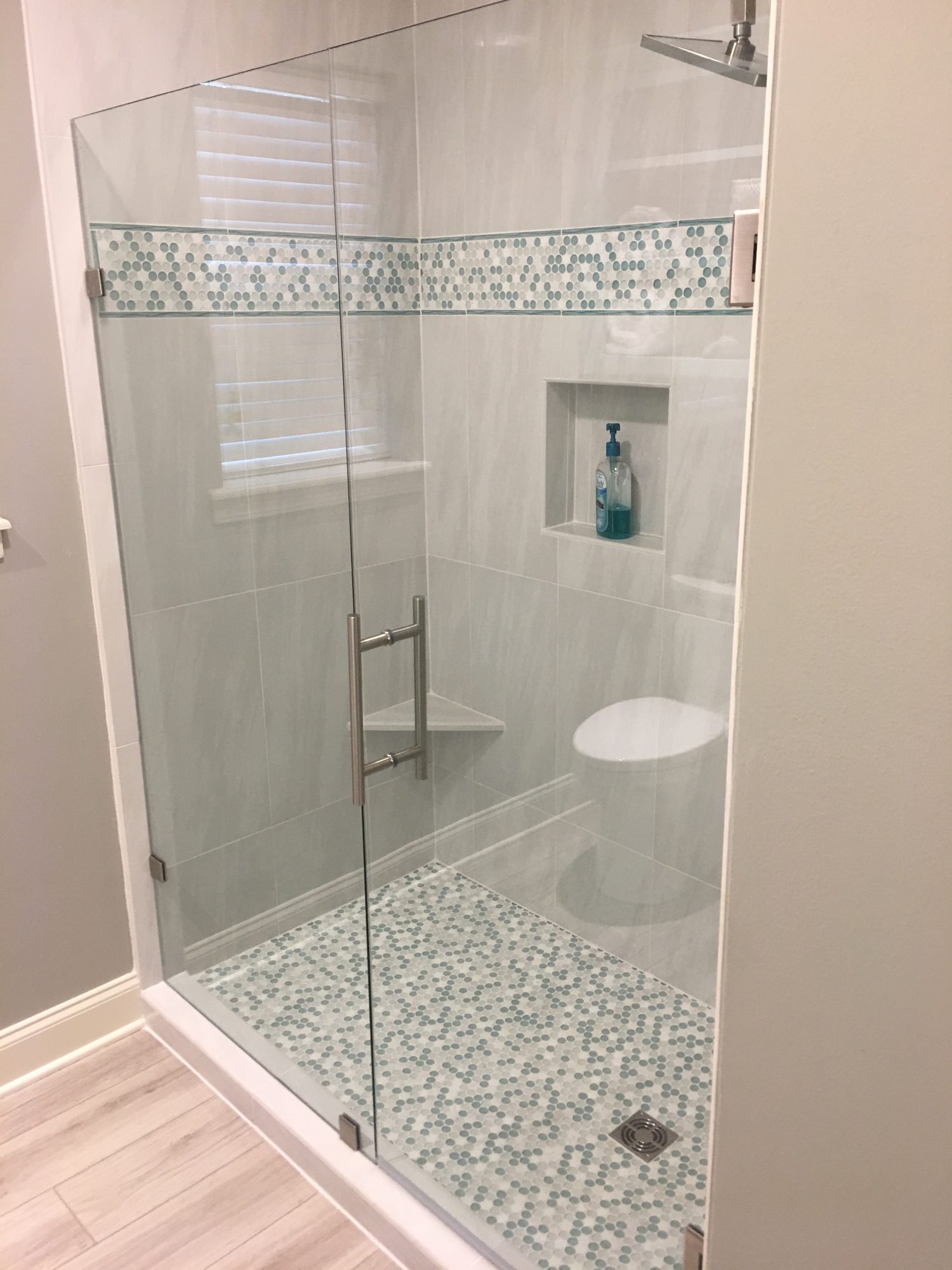 Walk-in shower with frameless glass enclosure, mosaic tile accent band and mosaic floor
