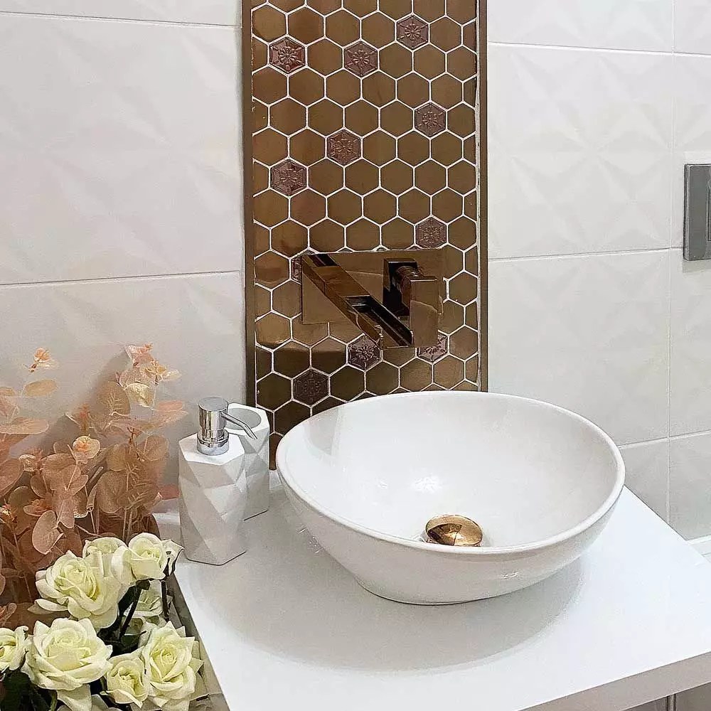 Bathroom tile ideas with metallic hexagon tiles used as an accent behind a white vessel sink, adding a bold and luxurious touch