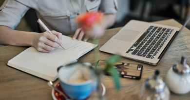 person writing on a notebook beside macbook
