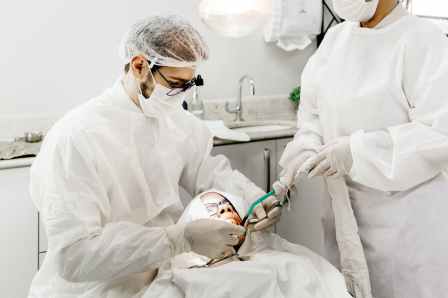 anonymous dentist with assistant treating teeth of patient