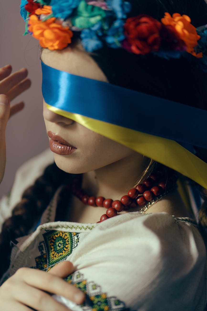 woman in slavic costume with eyes covered with ribbons in colours of the ukrainian flag