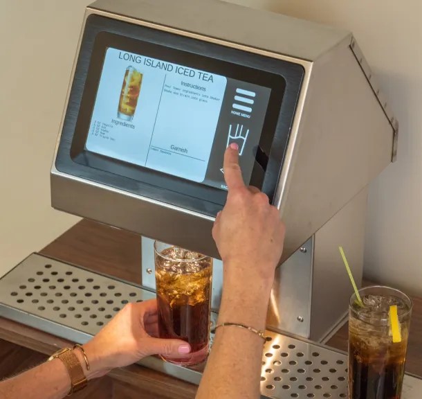 Touchscreen cocktail dispenser machine pouring a Long Island Iced Tea with recipe instructions on screen.