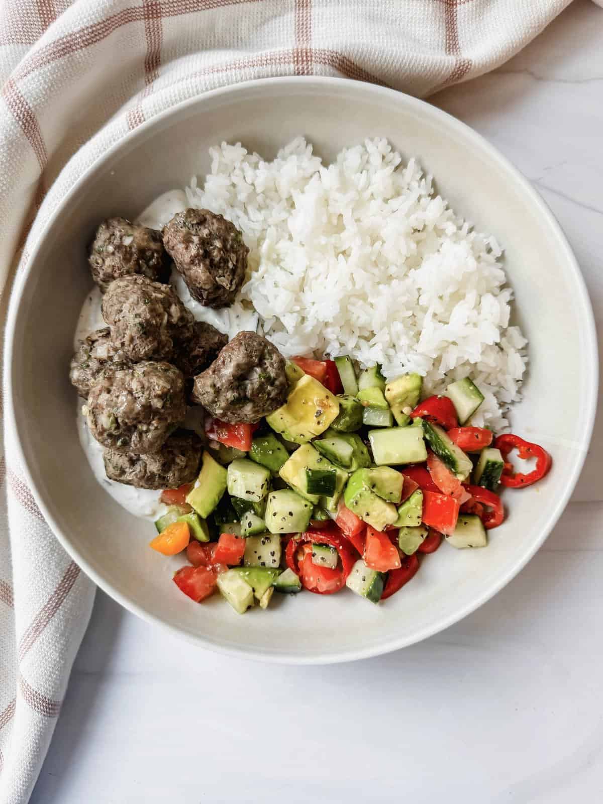 this is a top view of my lebanese-style kofta meatballs served with some white rice and an easy side salad on a bed of tzatziki sauce. 