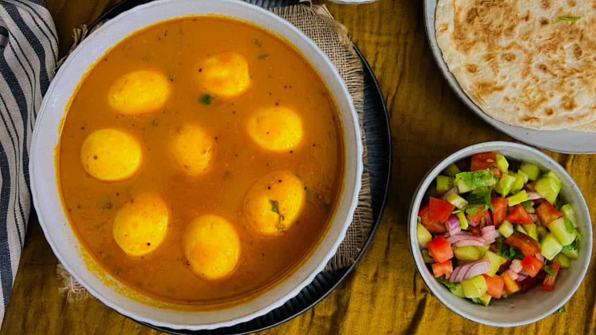 Egg curry in a white bowl served with roti and kachumber.