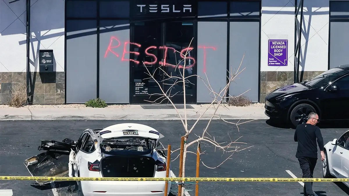 Burned and broken Tesla in front of a vandalized Tesla showroom