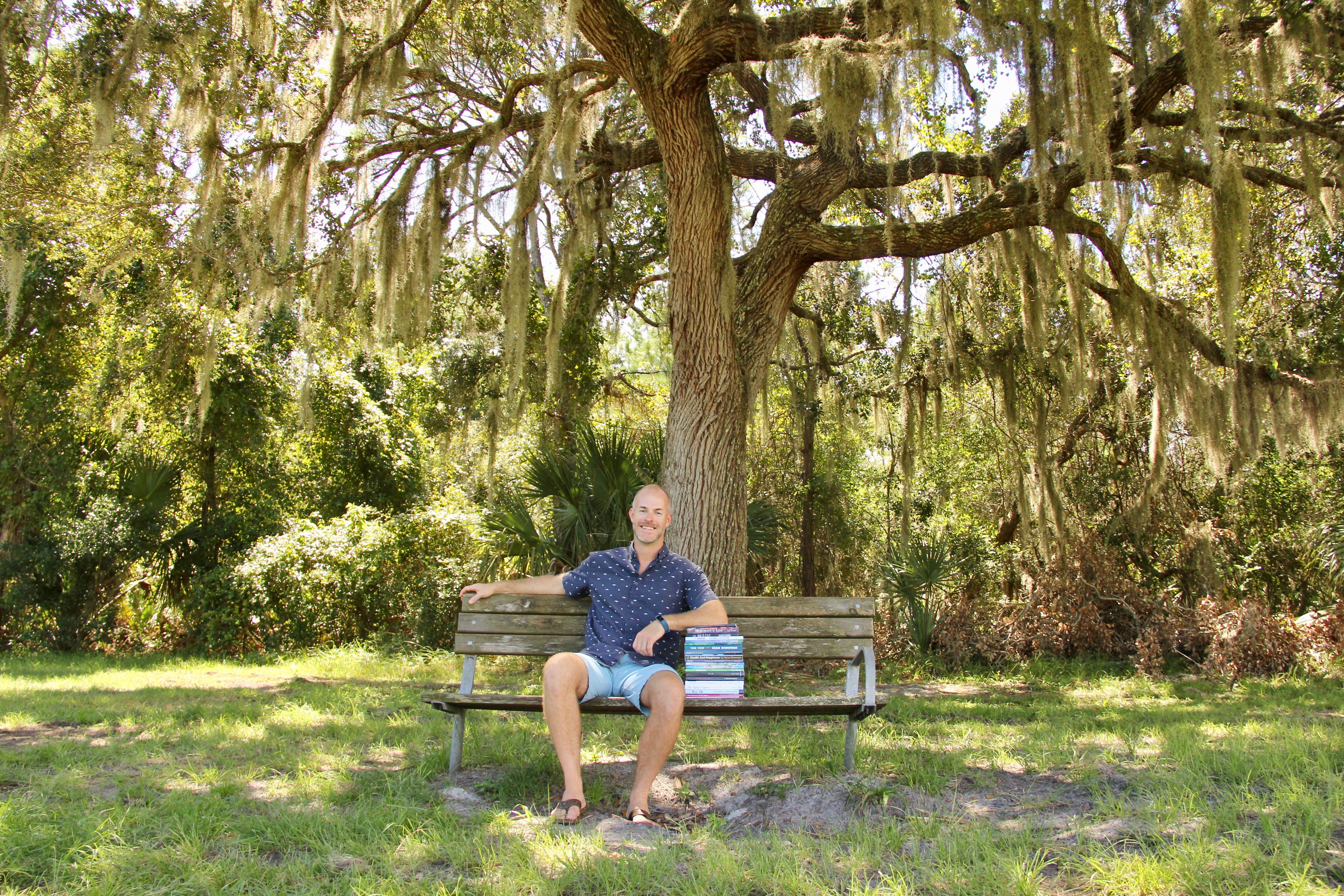 Author, Sean Donavan, sits under tree with stack of published books