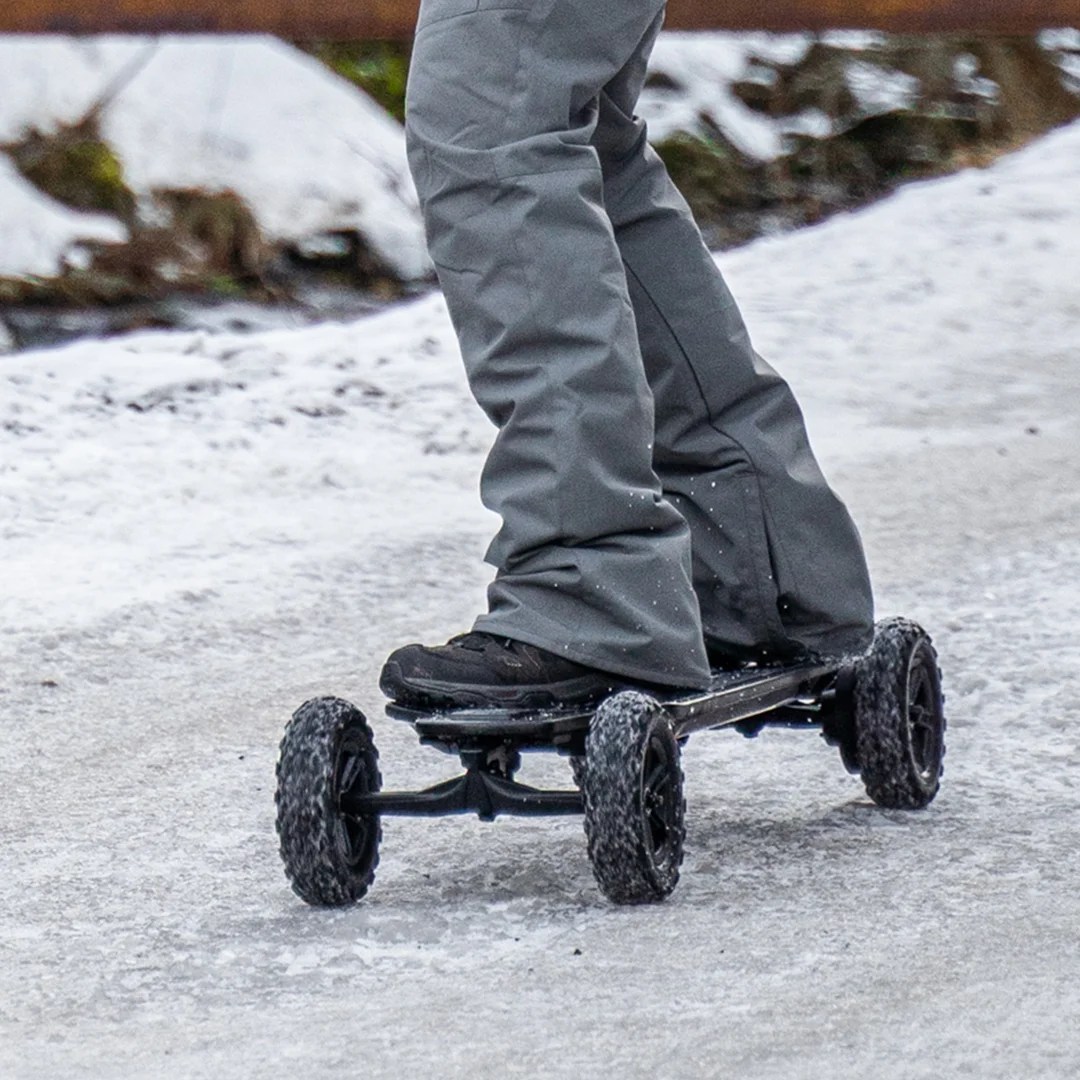 Exway Atlas Carbon elektriline longboard, millel on neli ratast ja must raam, sõitja peal jääteel.