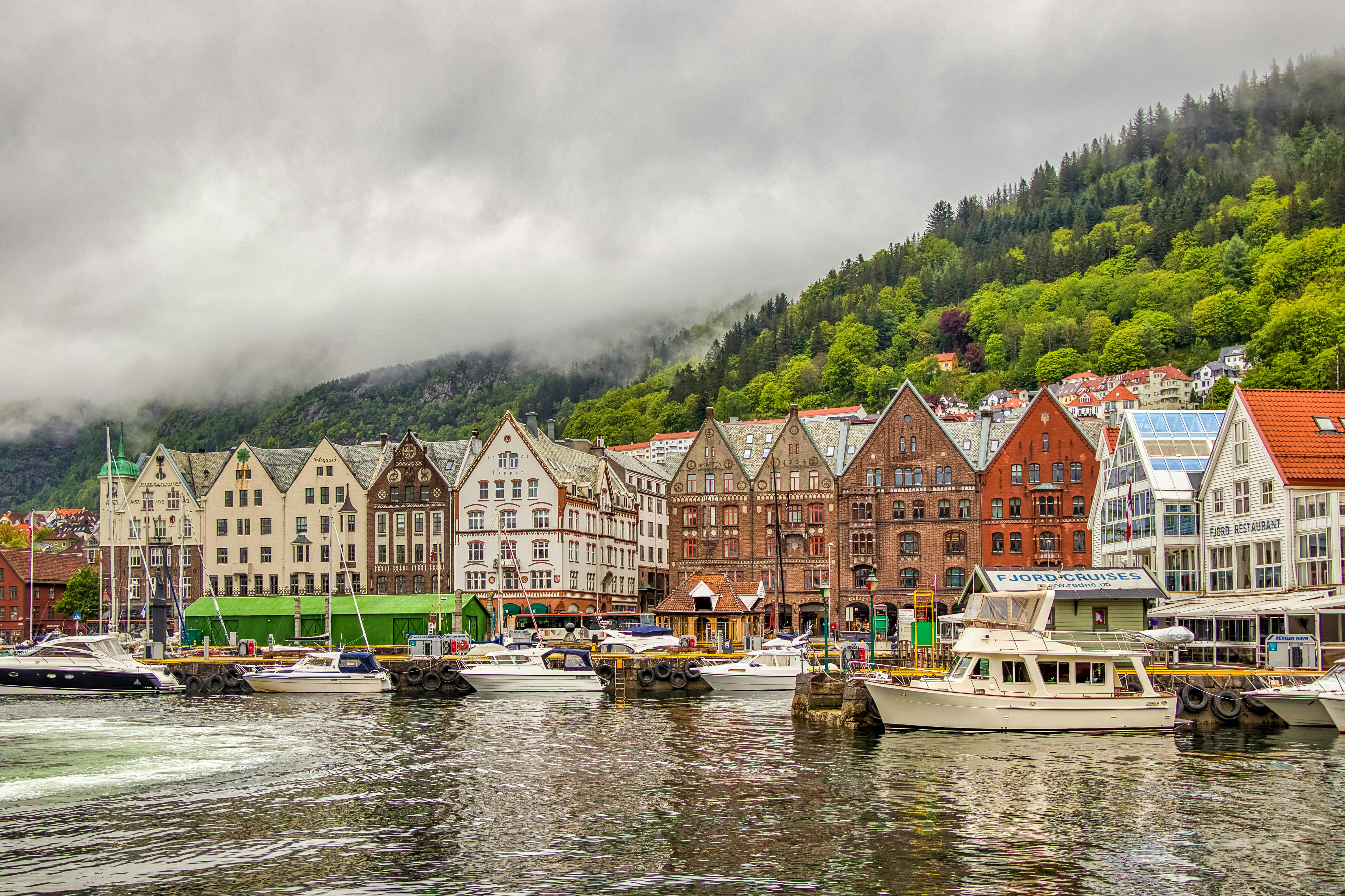 Colorful historic buildings line Bergen harbor with boats and misty mountains in background, Norway
