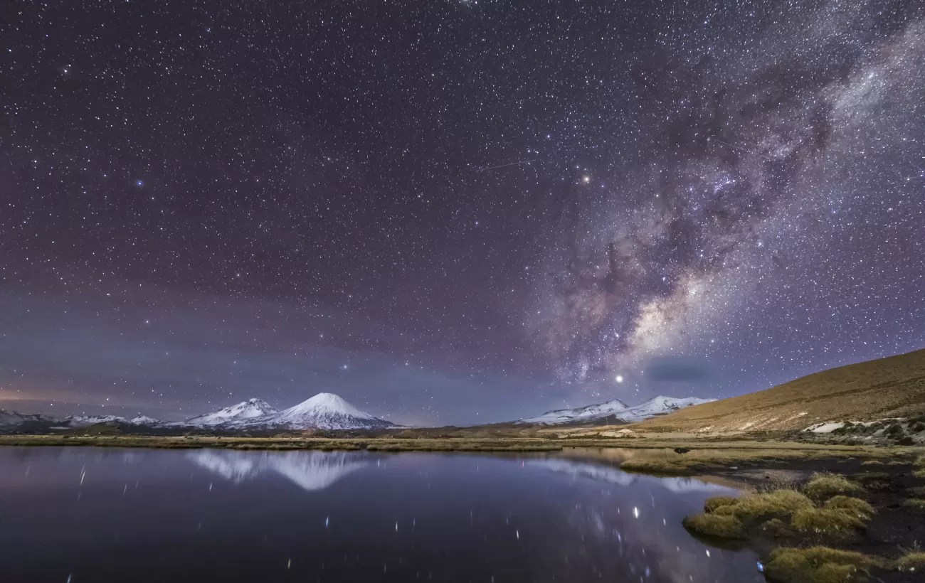 Milky Way galaxy over snow-capped Andes mountains reflected in pristine Atacama Desert lagoon at night