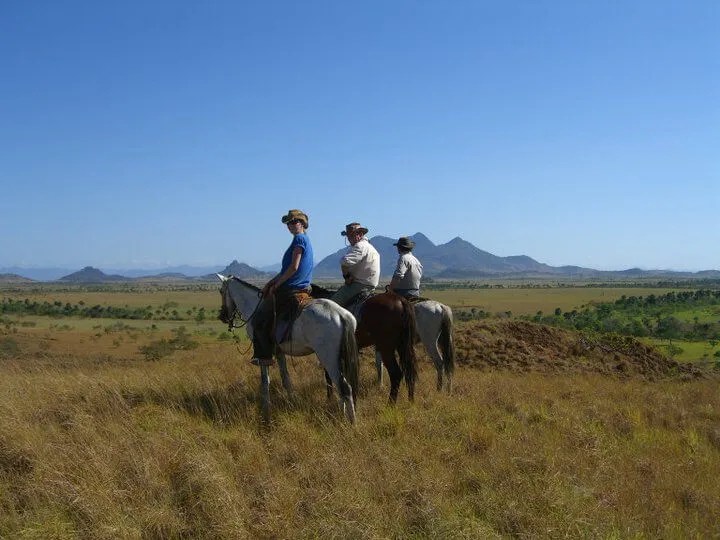 Three horseback riders overlooking vast Rupununi savanna grasslands with mountains in distance