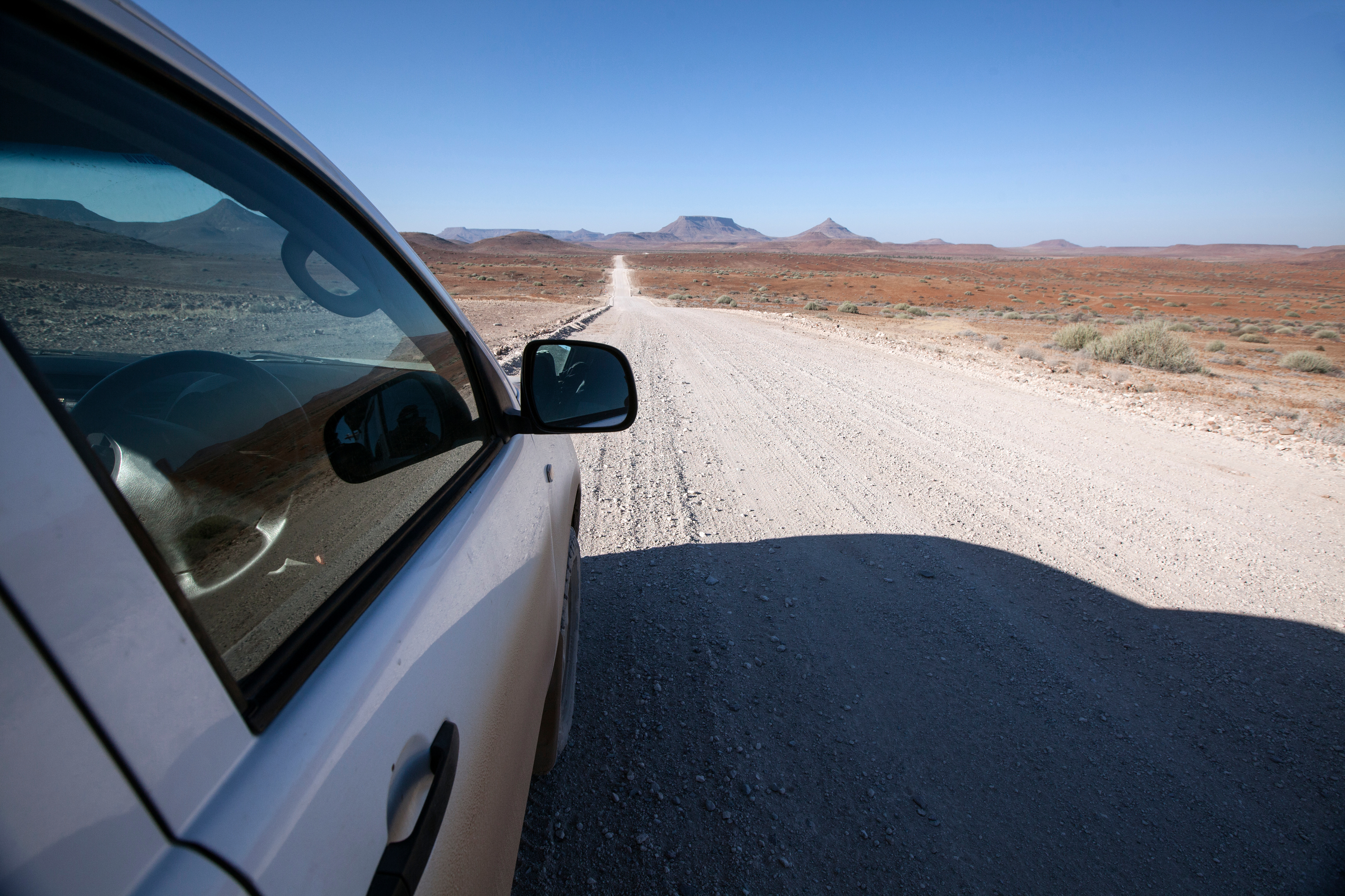 View from inside a vehicle on a gravel road in Damaraland, Namibia, with flat-topped mountains on the horizon