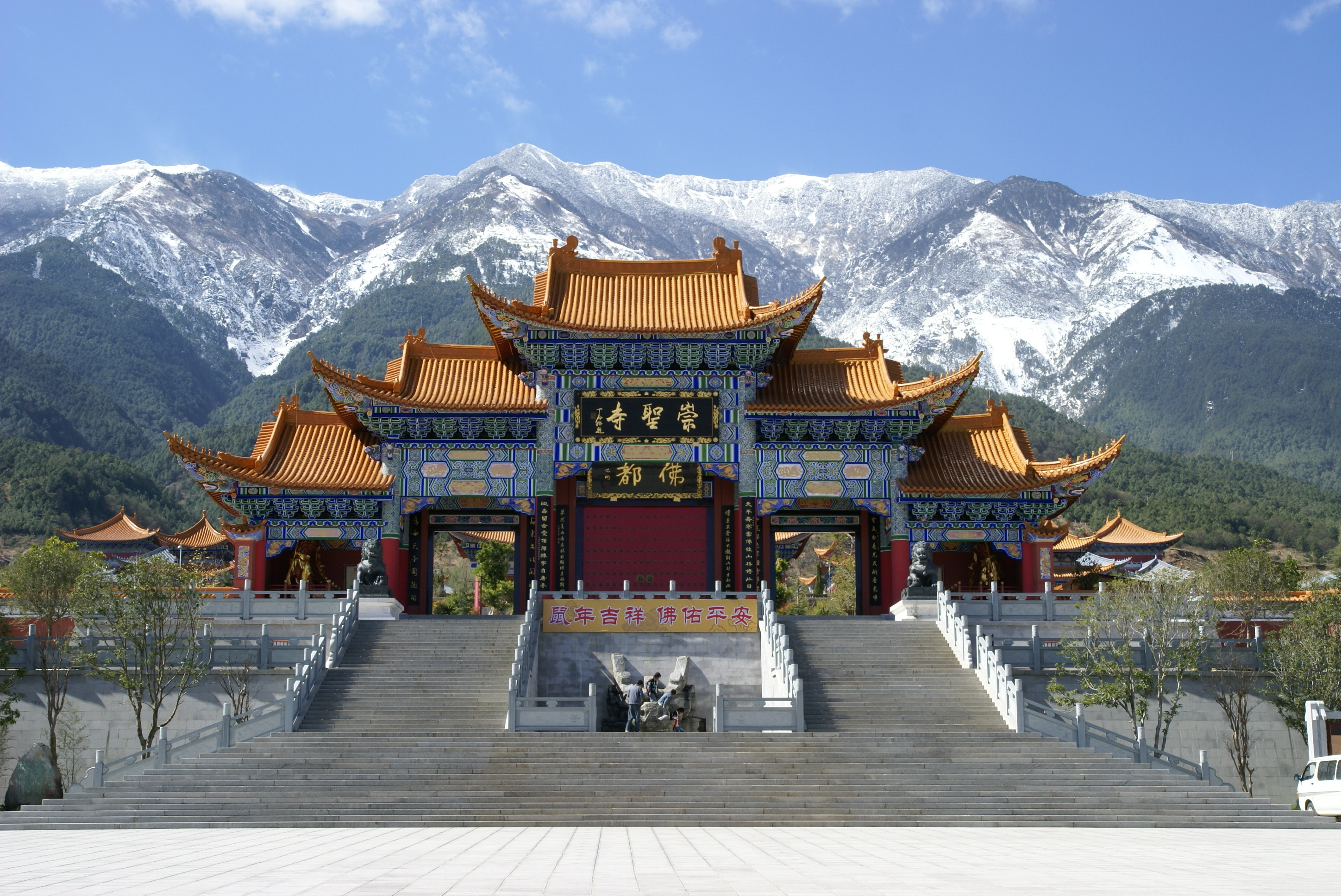 Ornate gateway of Chongsheng Temple with golden tiled roofs and snow capped Cangshan mountains rising behind, Dali, Yunnan