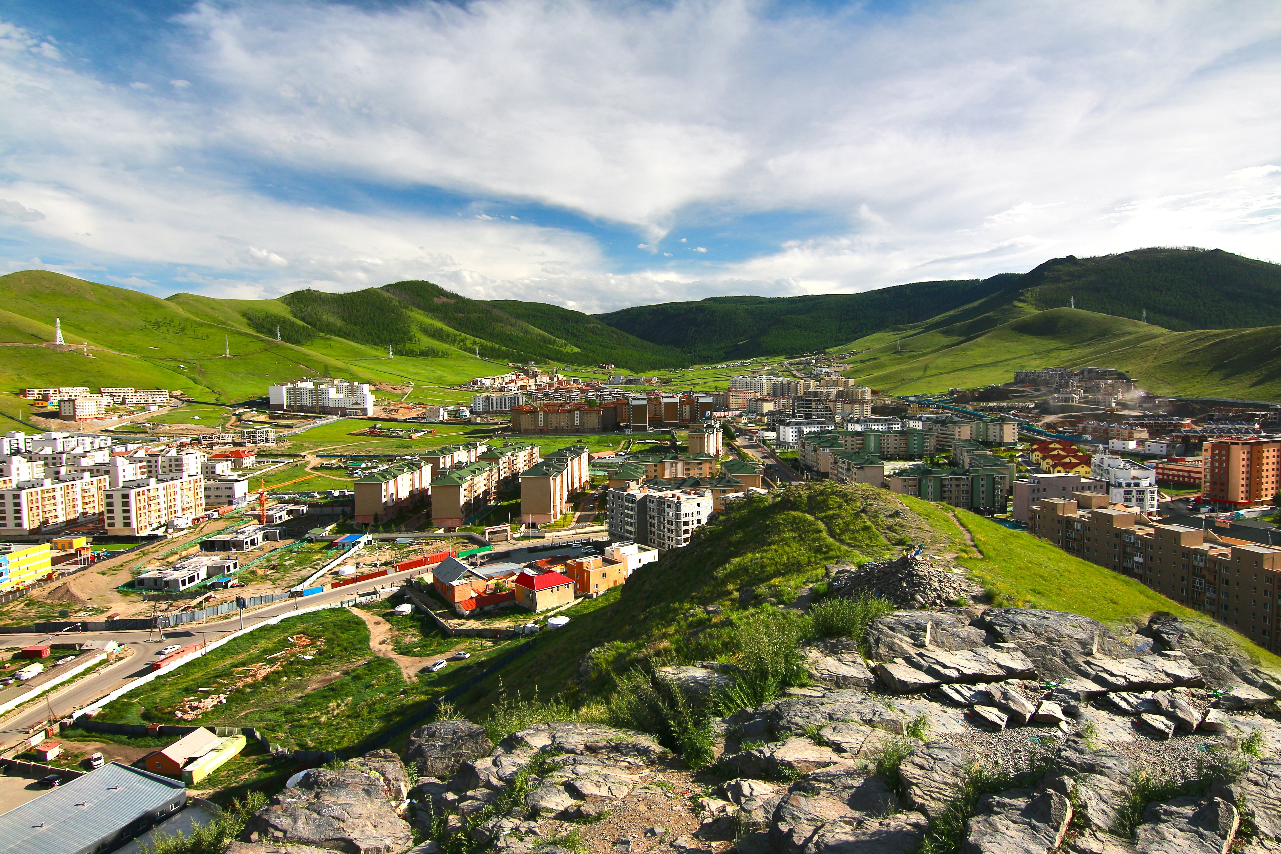 Aerial view of Ulaanbaatar's residential districts spreading across a green valley, with rocky hilltop outcrop in the foreground