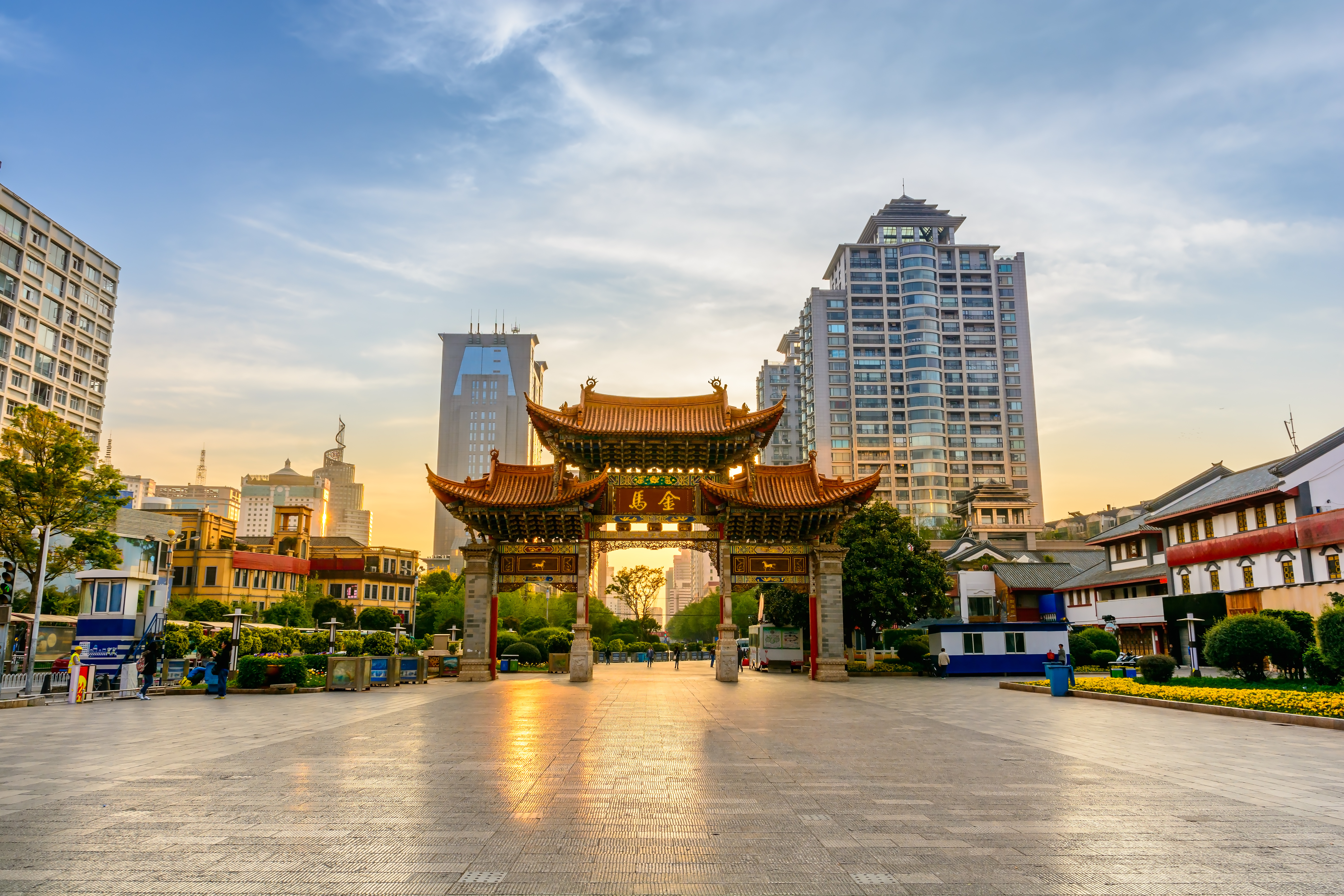 Jinma archway with gold rooftops stands in Jinbi Square, Kunming, against a backdrop of modern high-rise towers at sunrise