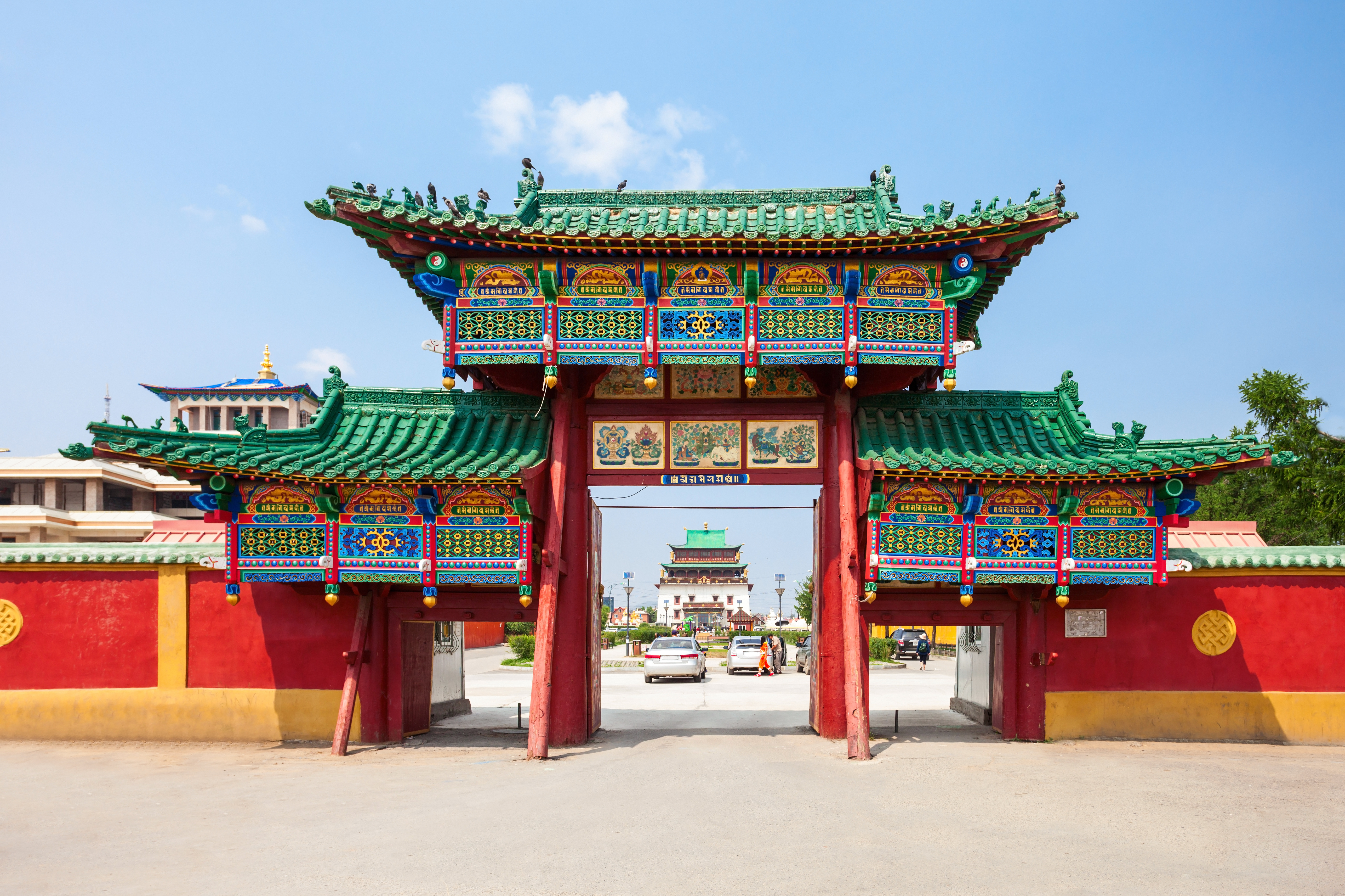 Ornate red and green painted gateway at Gandan Monastery in Ulaanbaatar, Mongolia, with a temple visible through the archway