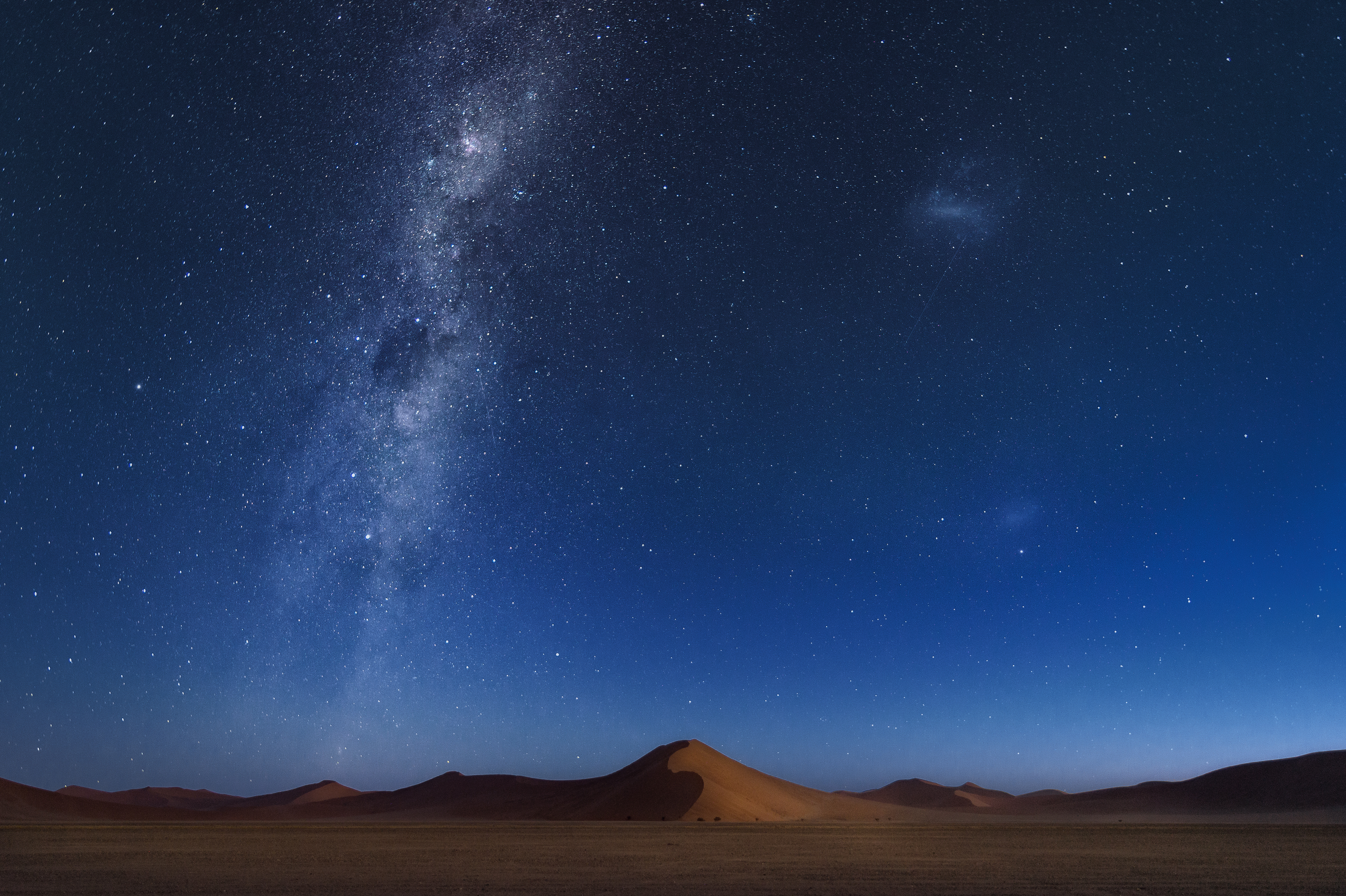 Star-filled night sky with the Milky Way arching over a curved red sand dune on the NamibRand plains, Namibia