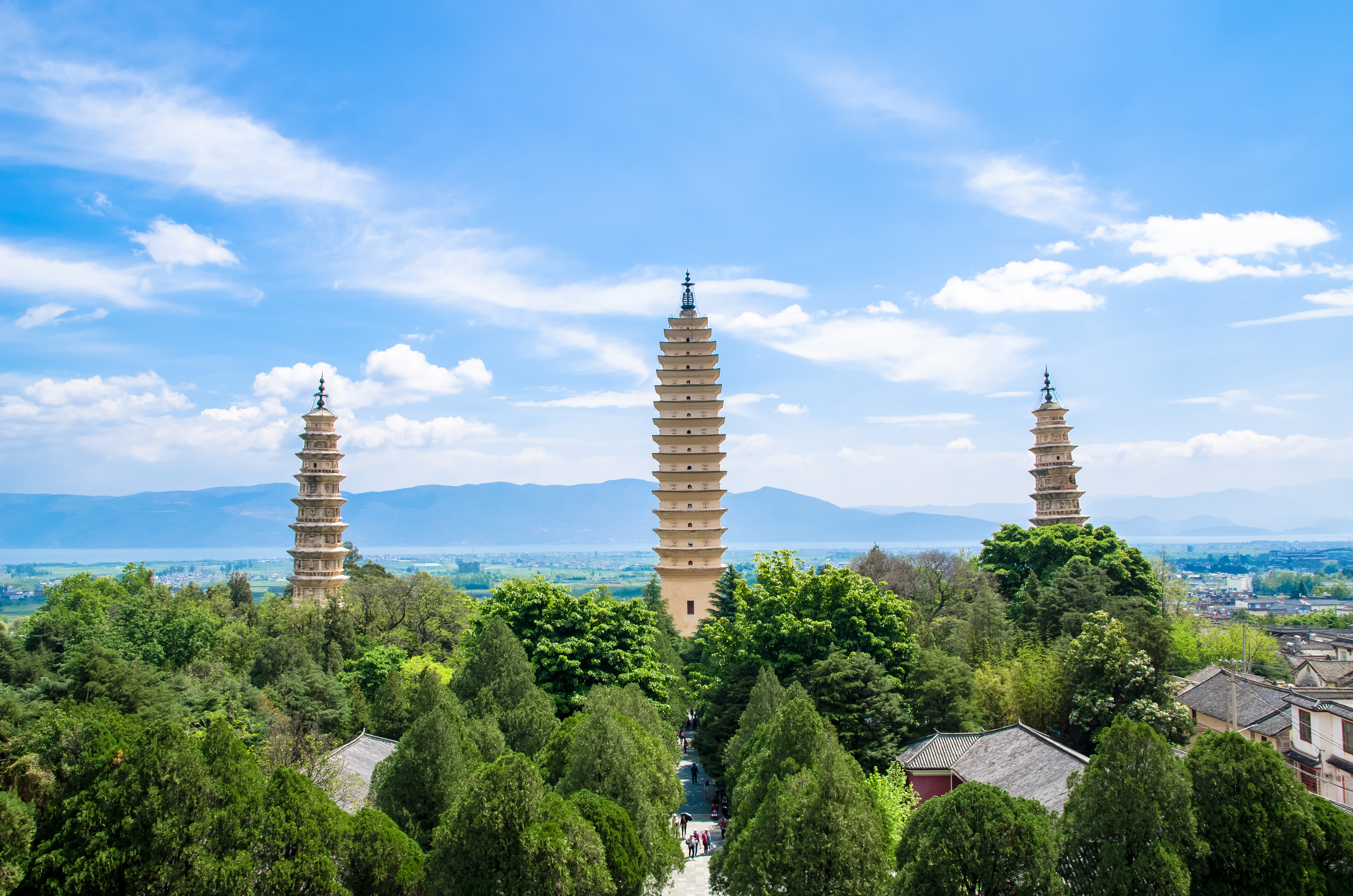 Three tiered pagodas of Chongsheng Temple rise above green trees near Dali, with mountains and a lake visible behind