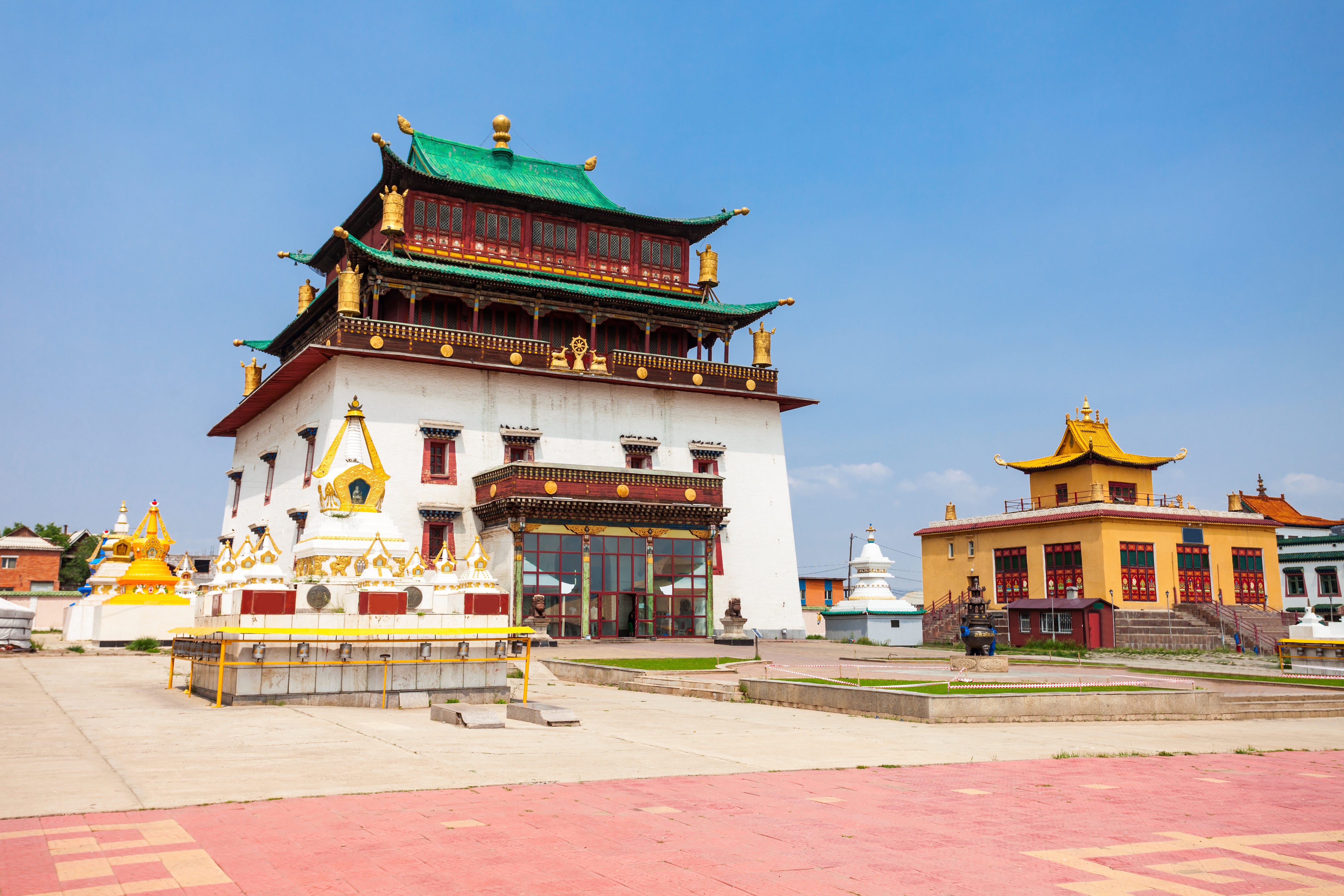 White and red multi-tiered temple with green tiered roof at Gandan Monastery, with golden stupas and a yellow temple building nearby in Ulaanbaatar
