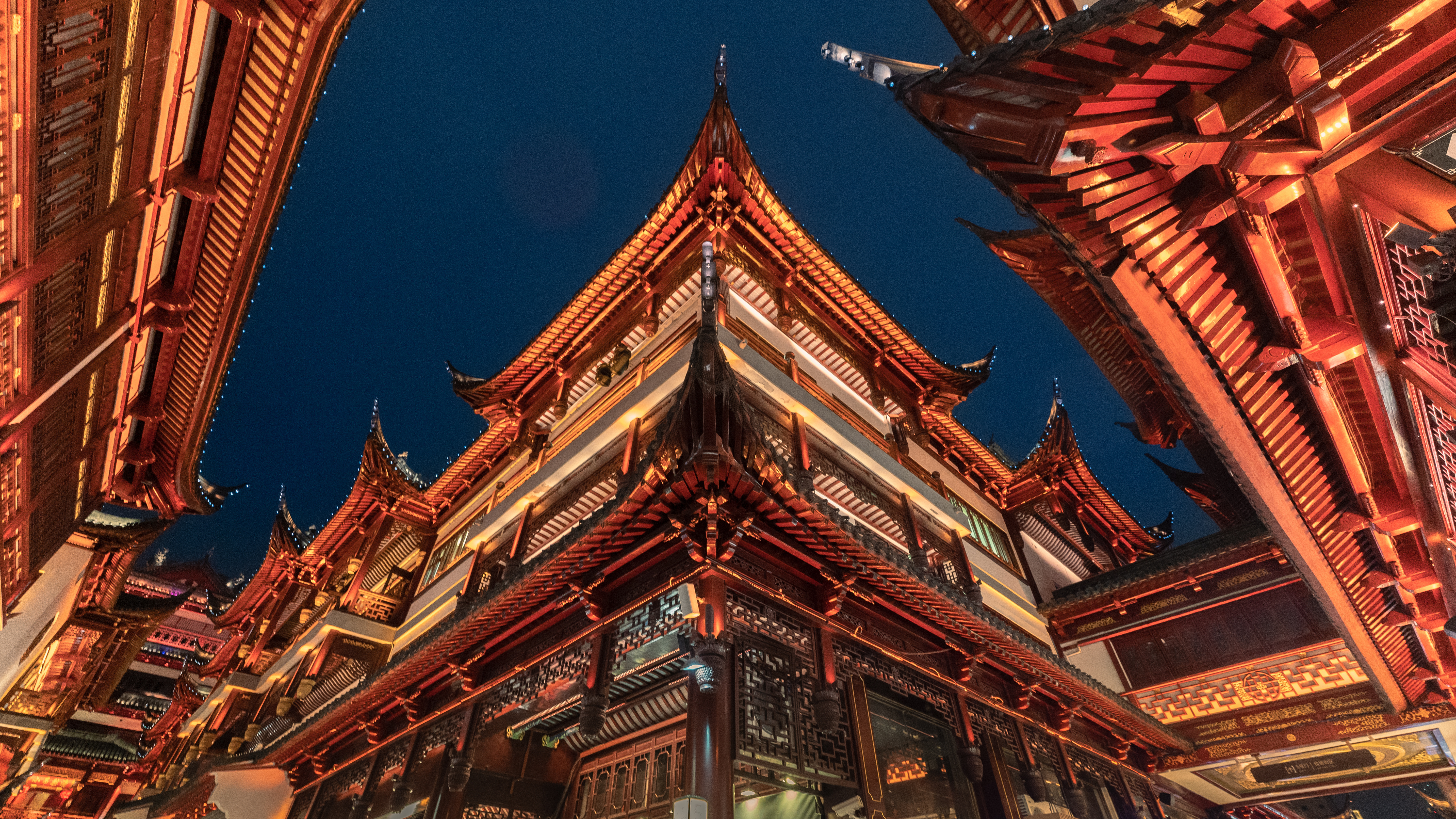 Upward view of tiered, upturned eaves at Yu Garden's old town buildings in Shanghai, lit red and gold against a night sky