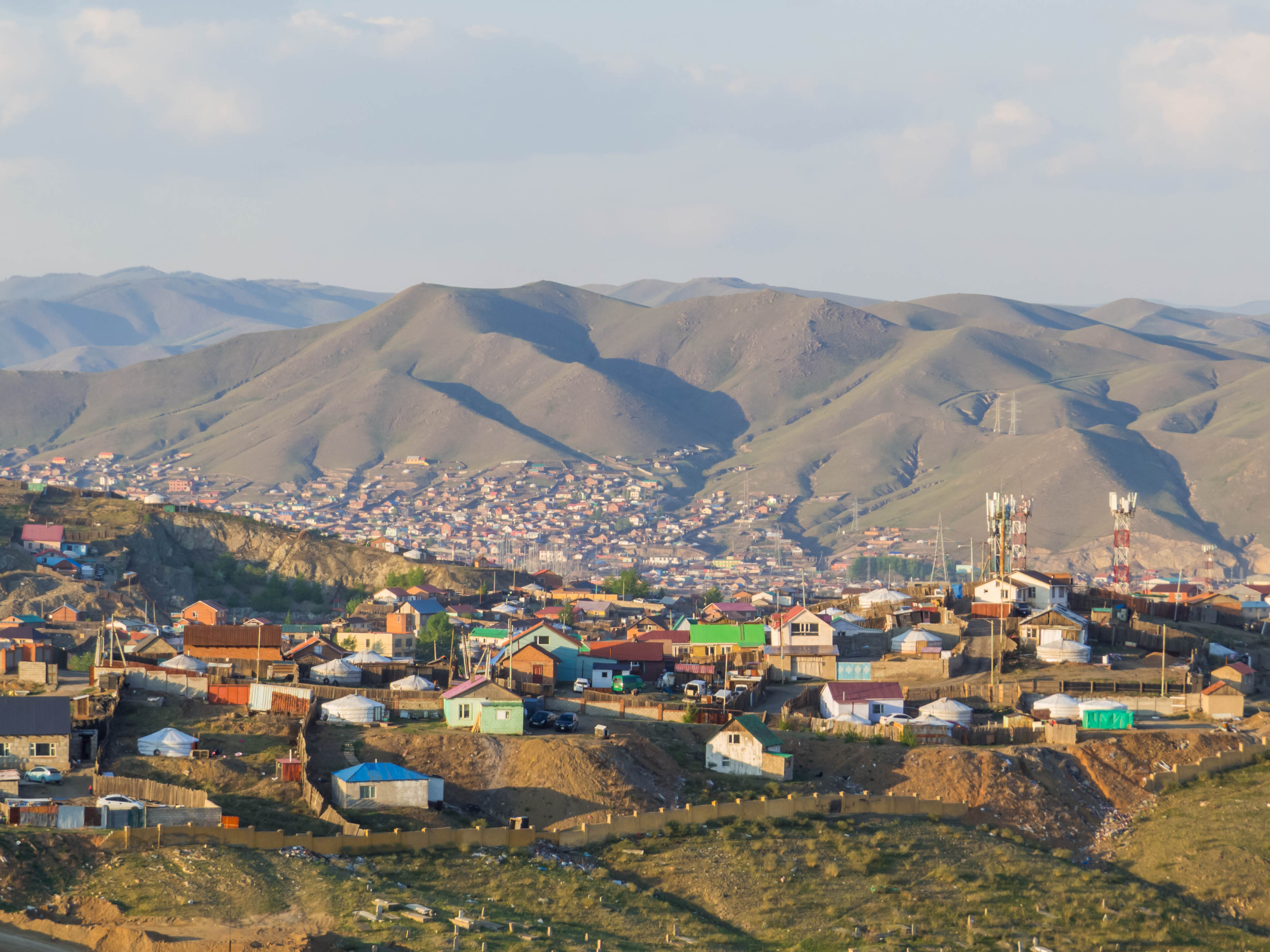 Ger district homes with colorful roofs spread across hillsides on the edge of Ulaanbaatar, with bare mountains behind