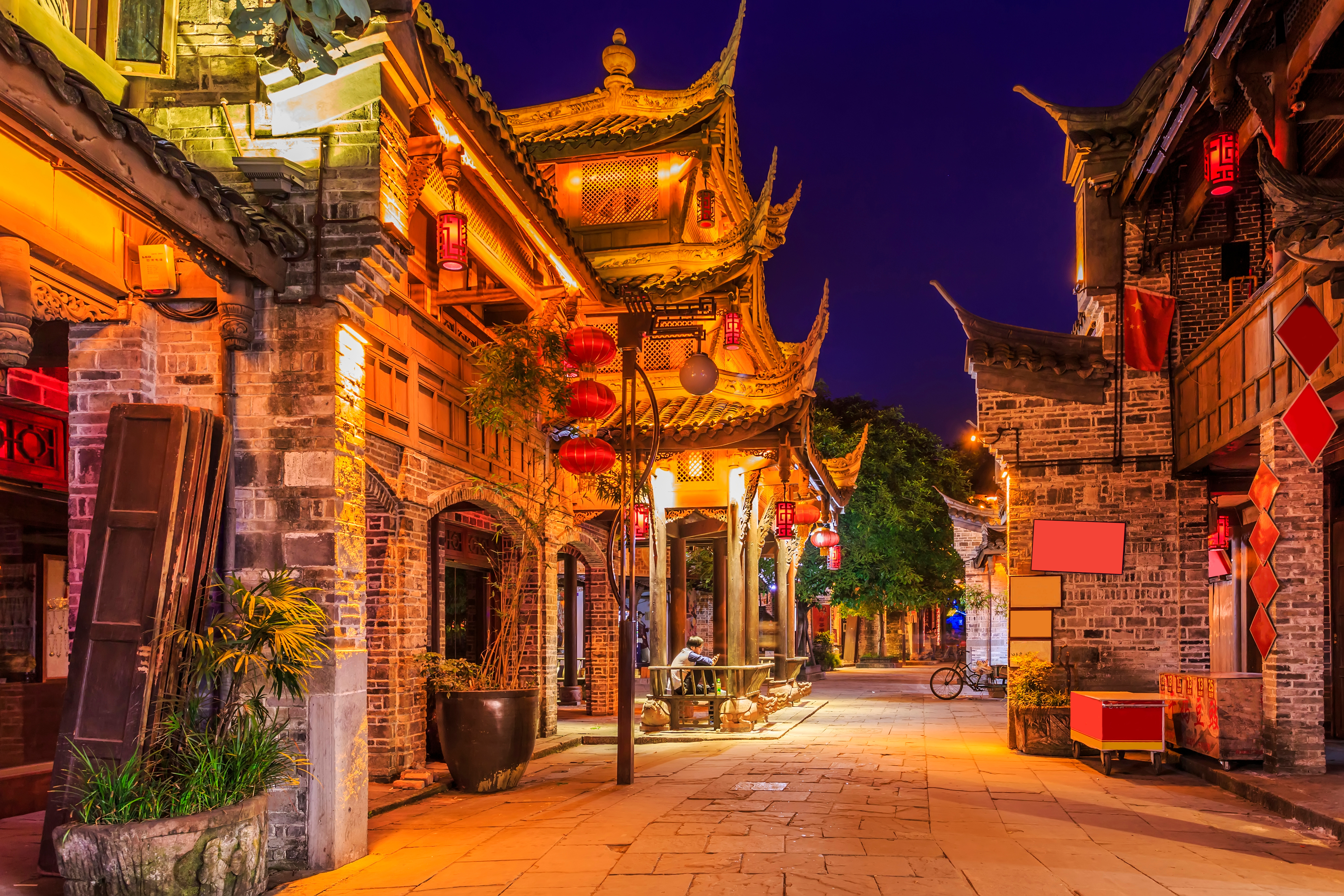 Illuminated ancient town street in Sichuan at night, with tiered wooden eaves, red lanterns and stone-paved lane lined with brick buildings