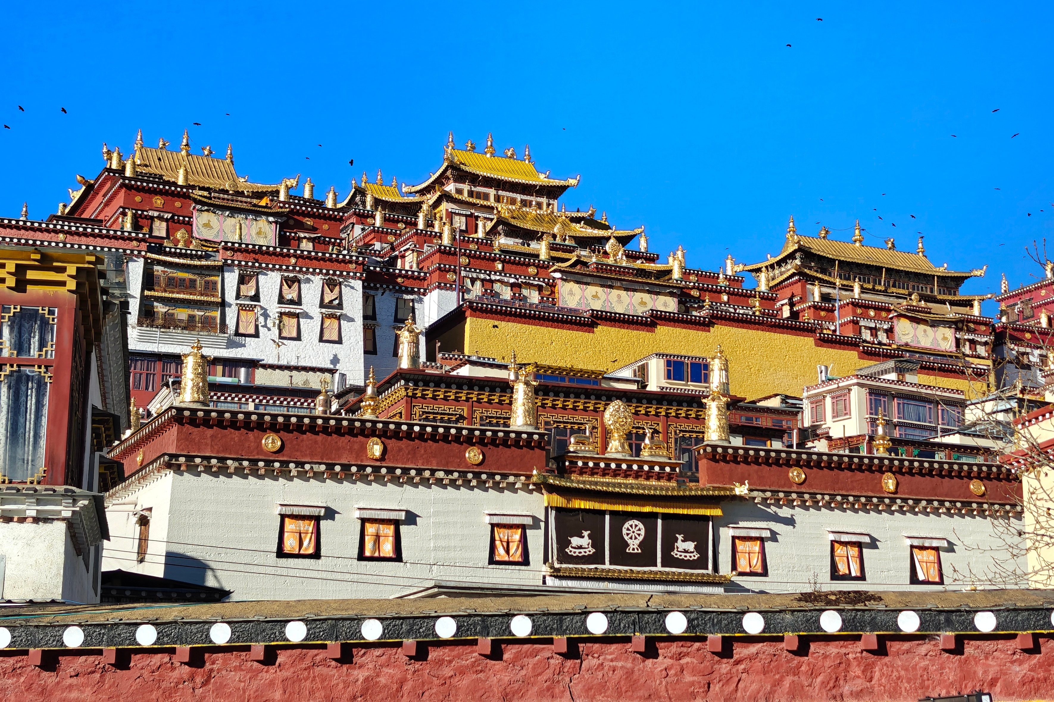 Tiered golden rooflines and red-walled buildings of Songzanlin Monastery rise against a clear blue sky in Shangri-La, Yunnan