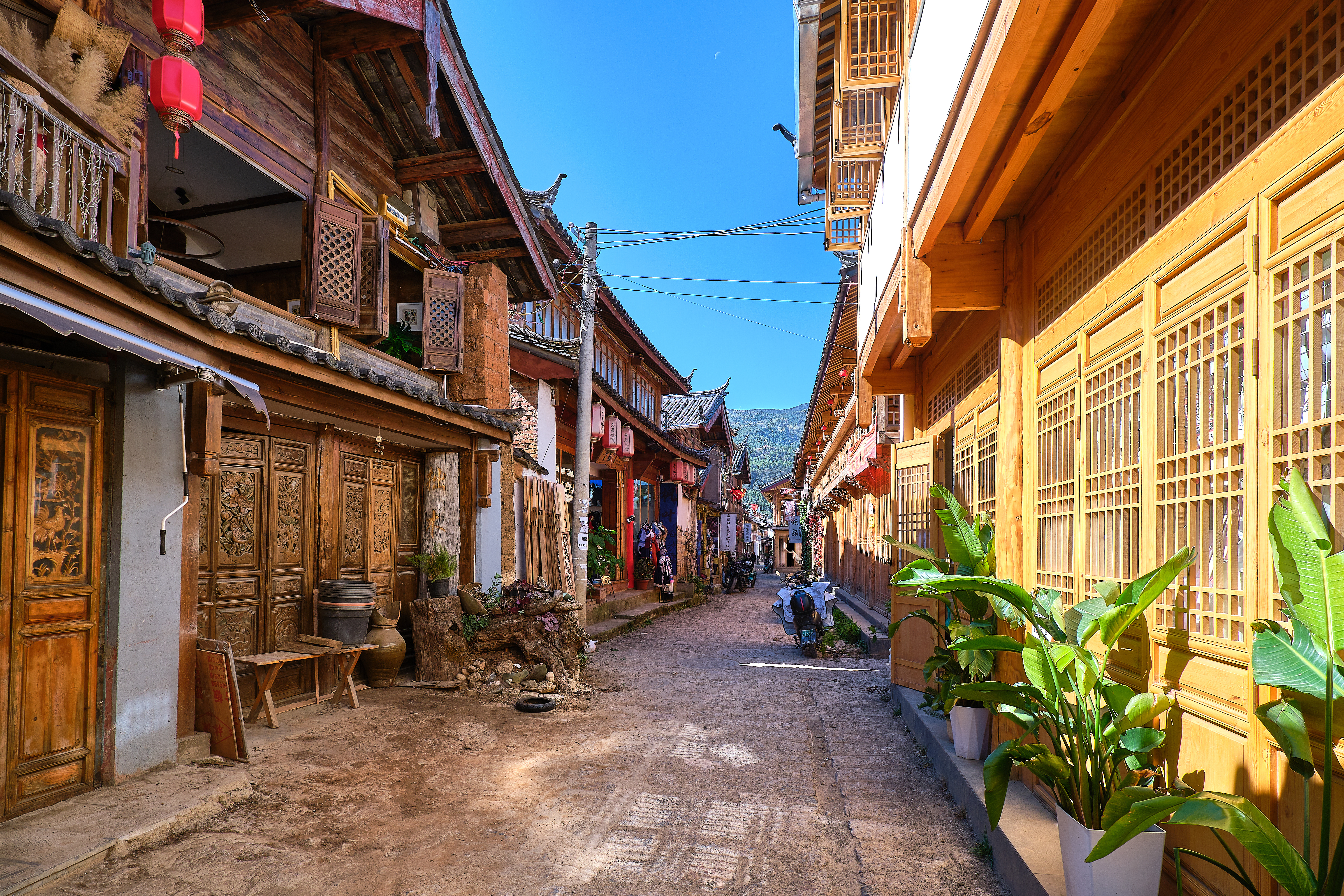 Cobbled lane in Baisha old town lined with wooden houses, carved doors, hanging lanterns and potted plants