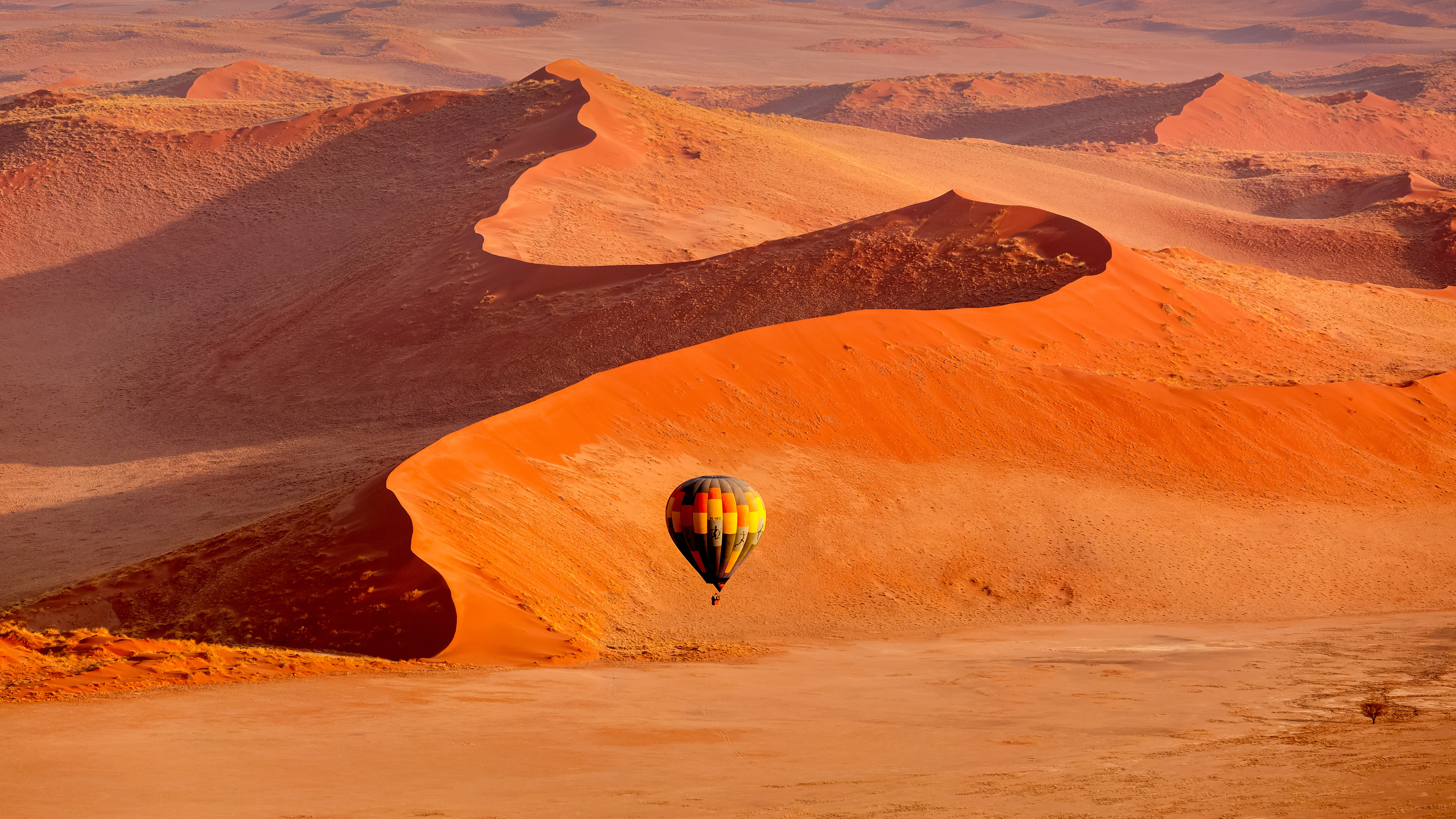 Hot air balloon drifting over the towering red sand dunes of Sossusvlei in Namibia at sunrise