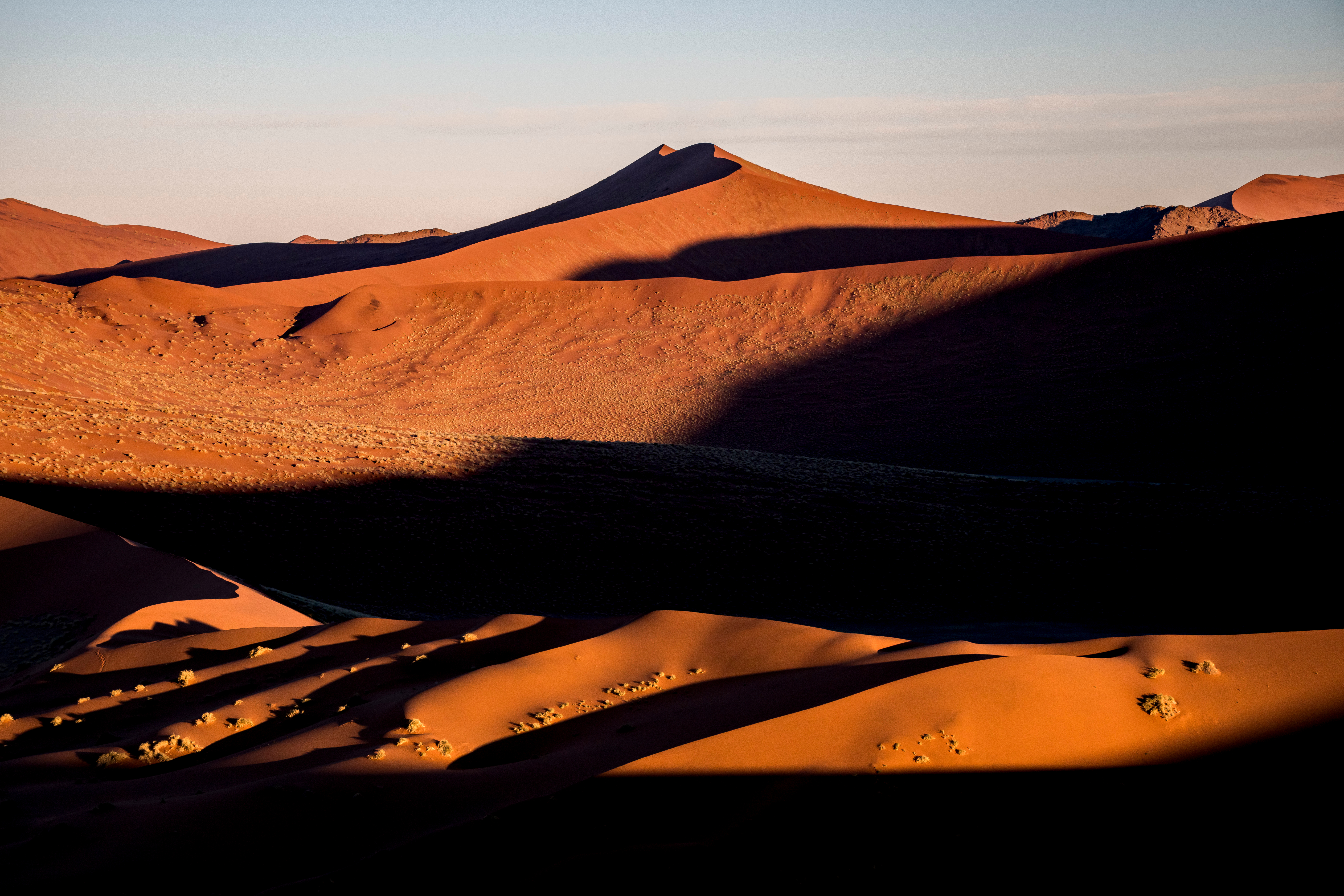 Sharp-ridged red sand dunes near Sossusvlei cast long dark shadows across the desert floor in early morning light