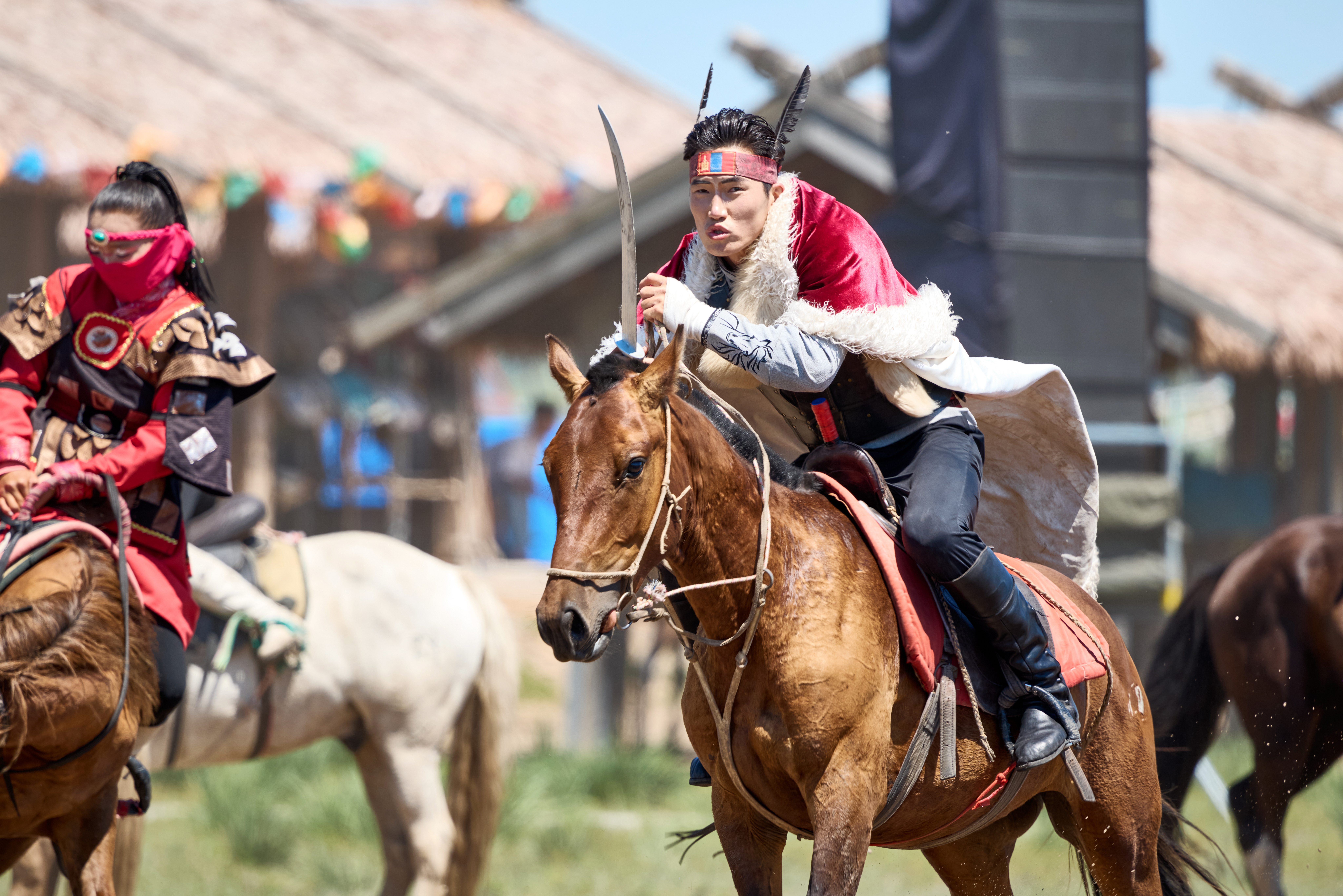 Costumed rider in a fur-trimmed cape brandishes a curved sword on horseback during a Naadam Festival performance in Mongolia
