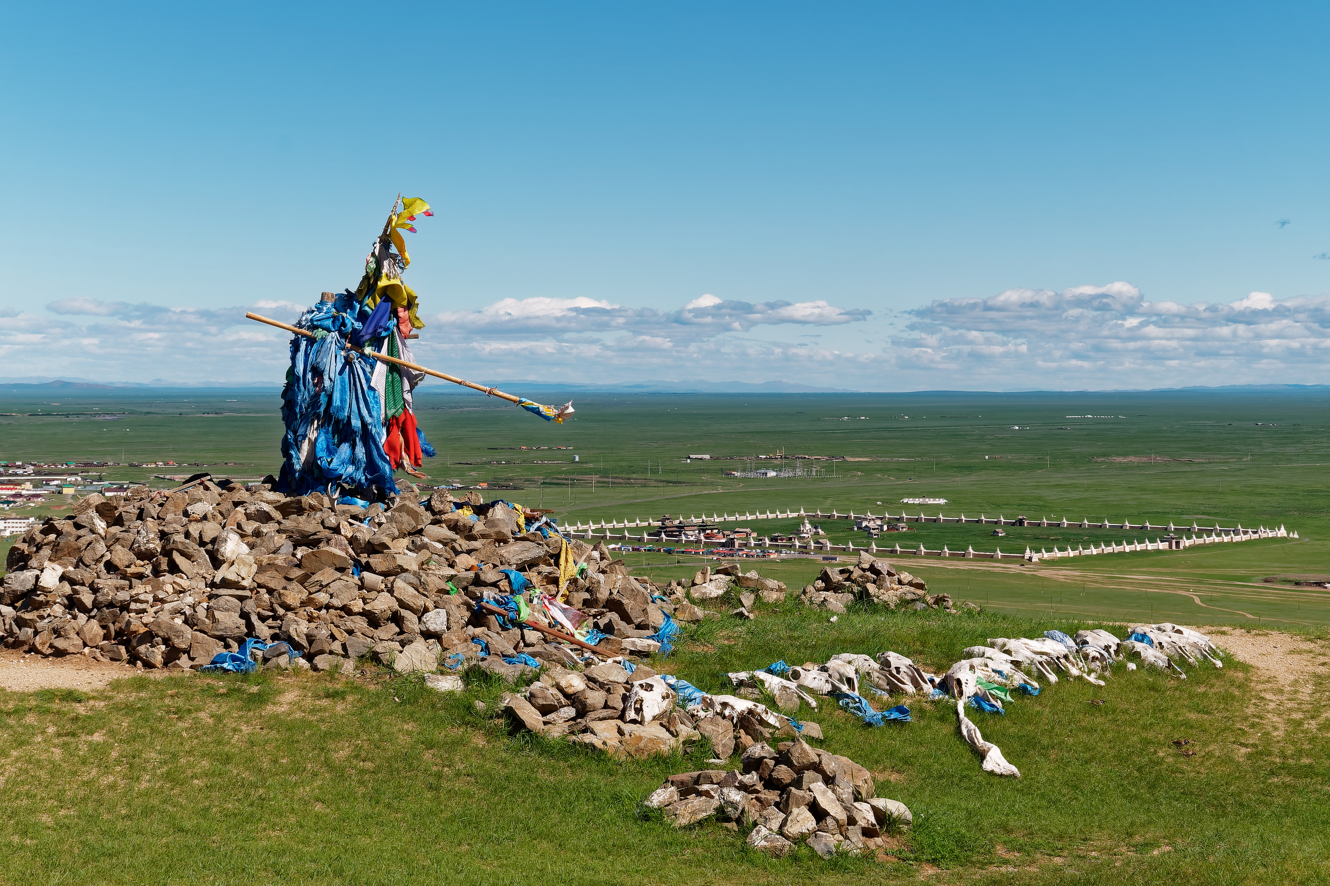 A stone ovoo shrine draped in blue prayer scarves and flags overlooks the walled Erdene Zuu monastery on the Karakorum steppe