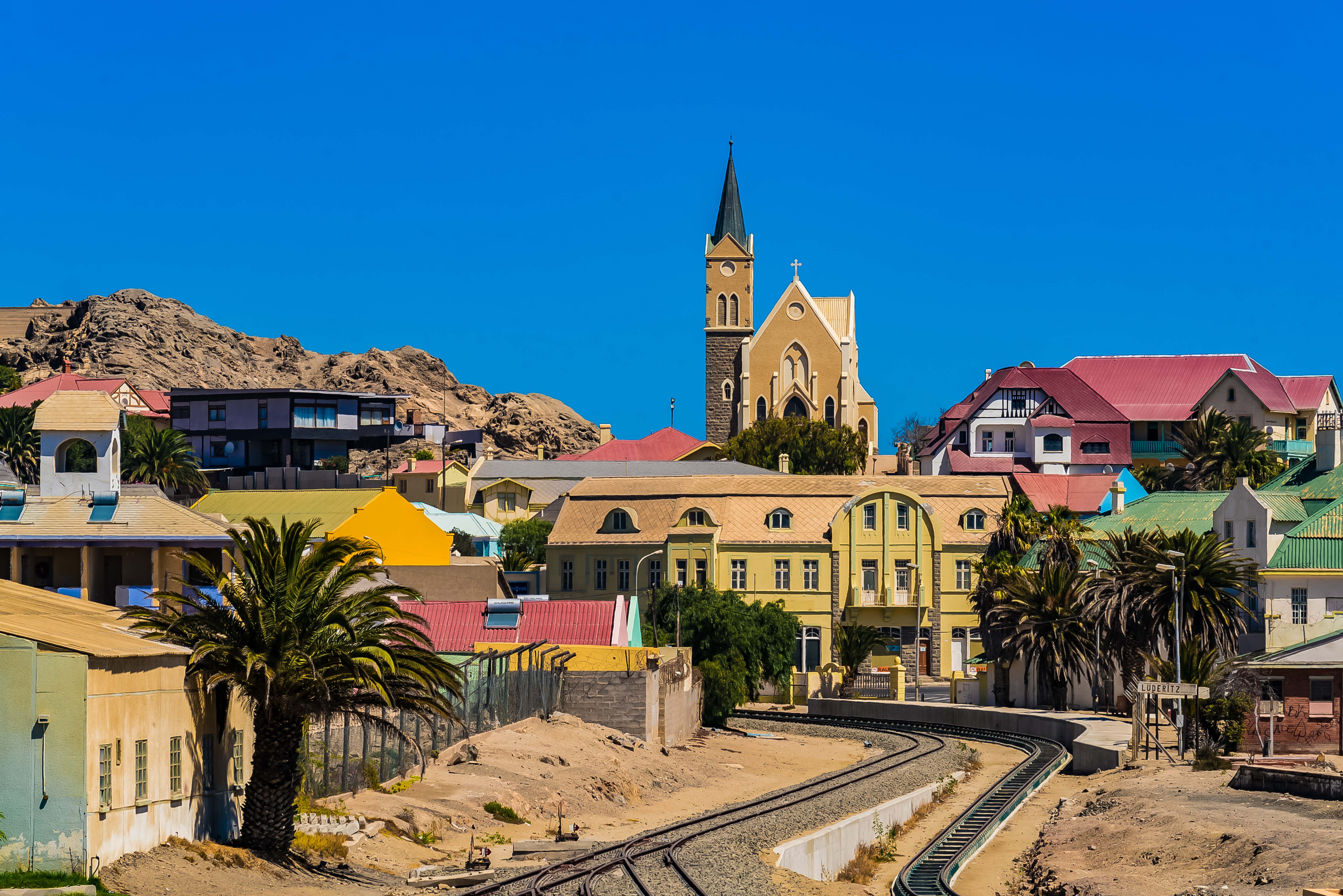 Luderitz skyline with the spired Lutheran church, colorful colonial buildings, palm trees and railway tracks curving toward the coast