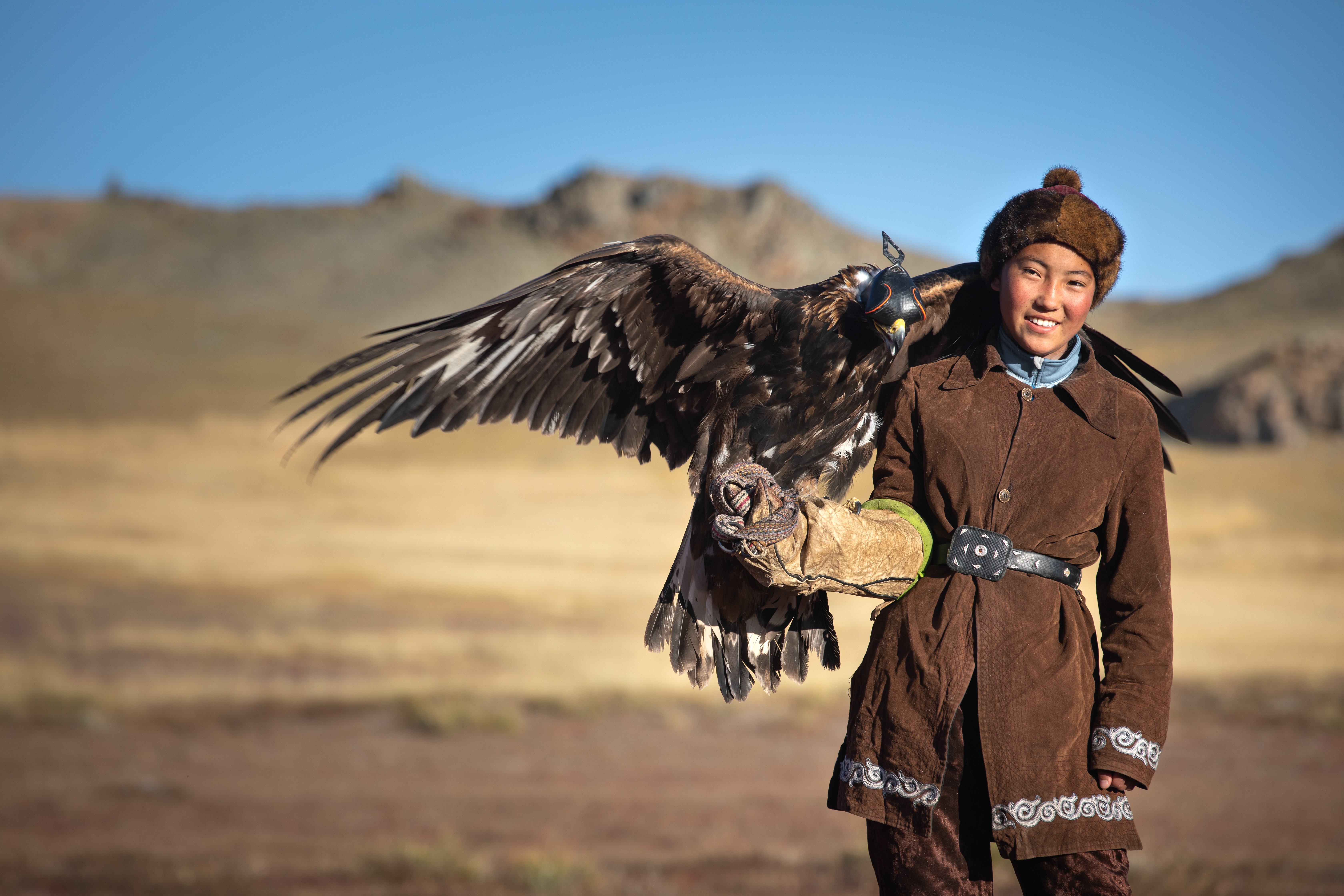 Kazakh eagle huntress in Ulgii, Western Mongolia, smiles while a golden eagle with spread wings perches on her gloved arm