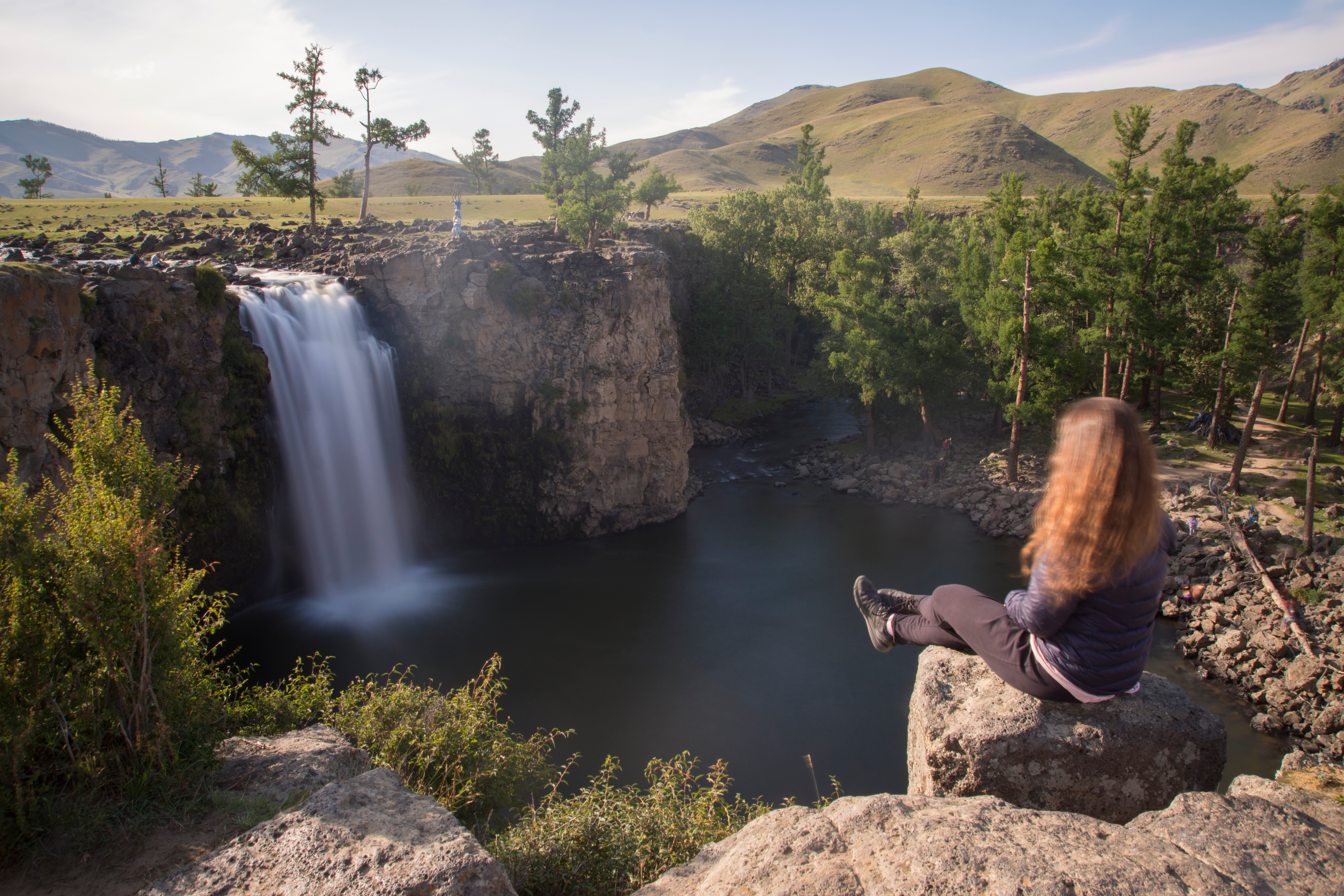 A visitor sits on a rock overlooking Ulaan Tsutgalan waterfall as it drops over basalt cliffs into a gorge in Mongolia's Orkhon Valley