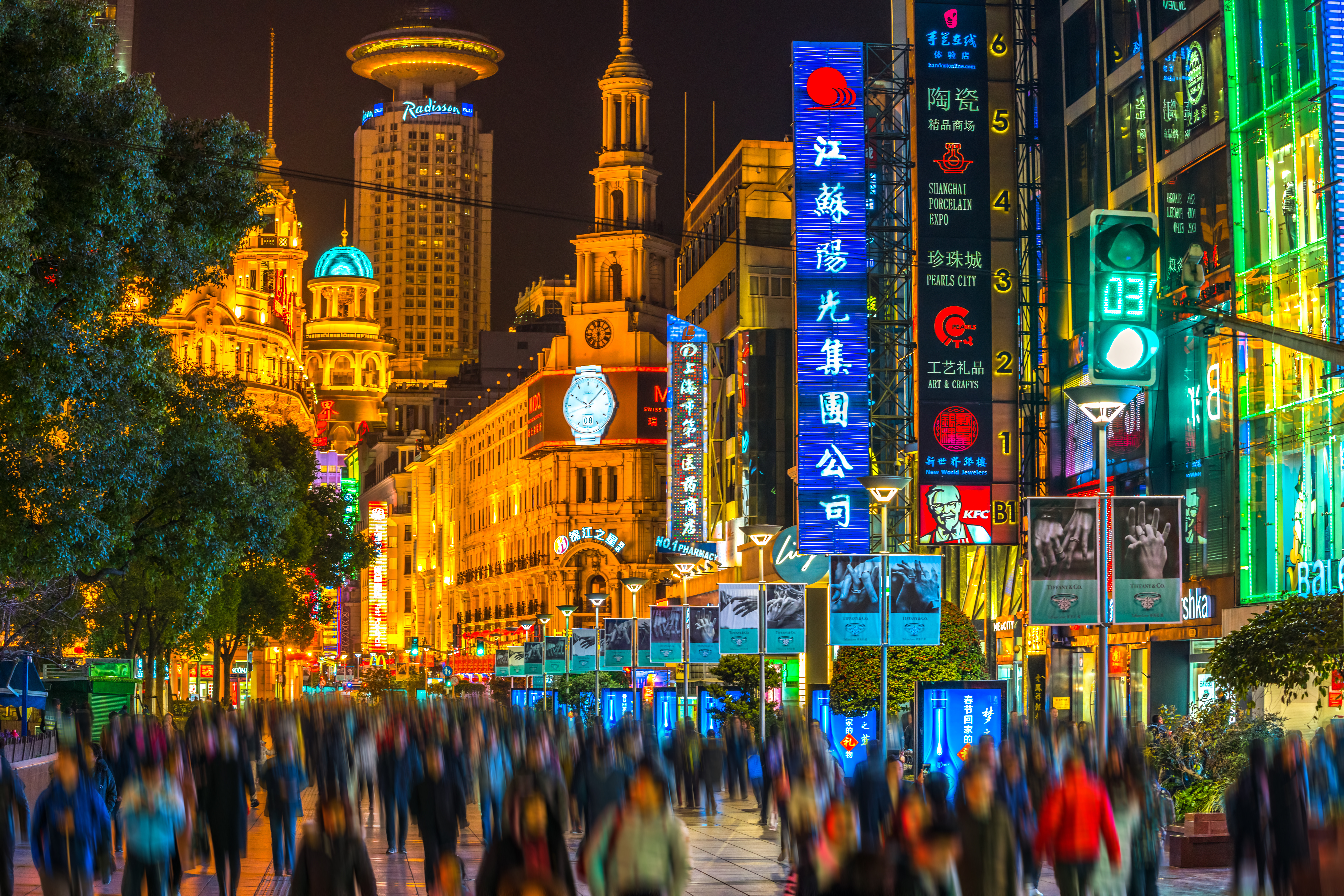 Illuminated neon signs and skyscrapers line Nanjing Road in Shanghai at night, with crowds of pedestrians filling the pedestrianized street below