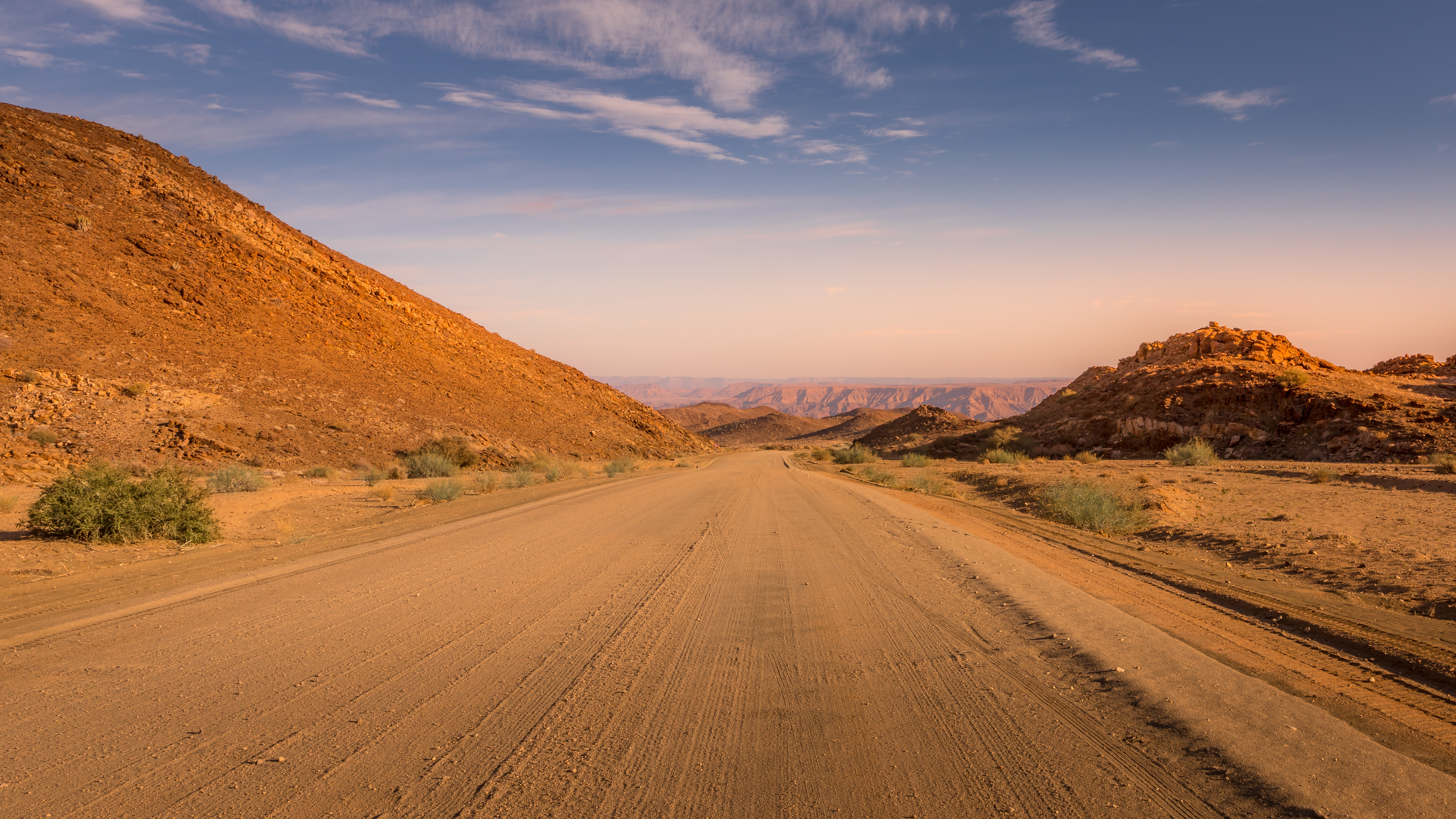 Gravel road running between red rocky hills near the Fish River Canyon area of southern Namibia at sunset