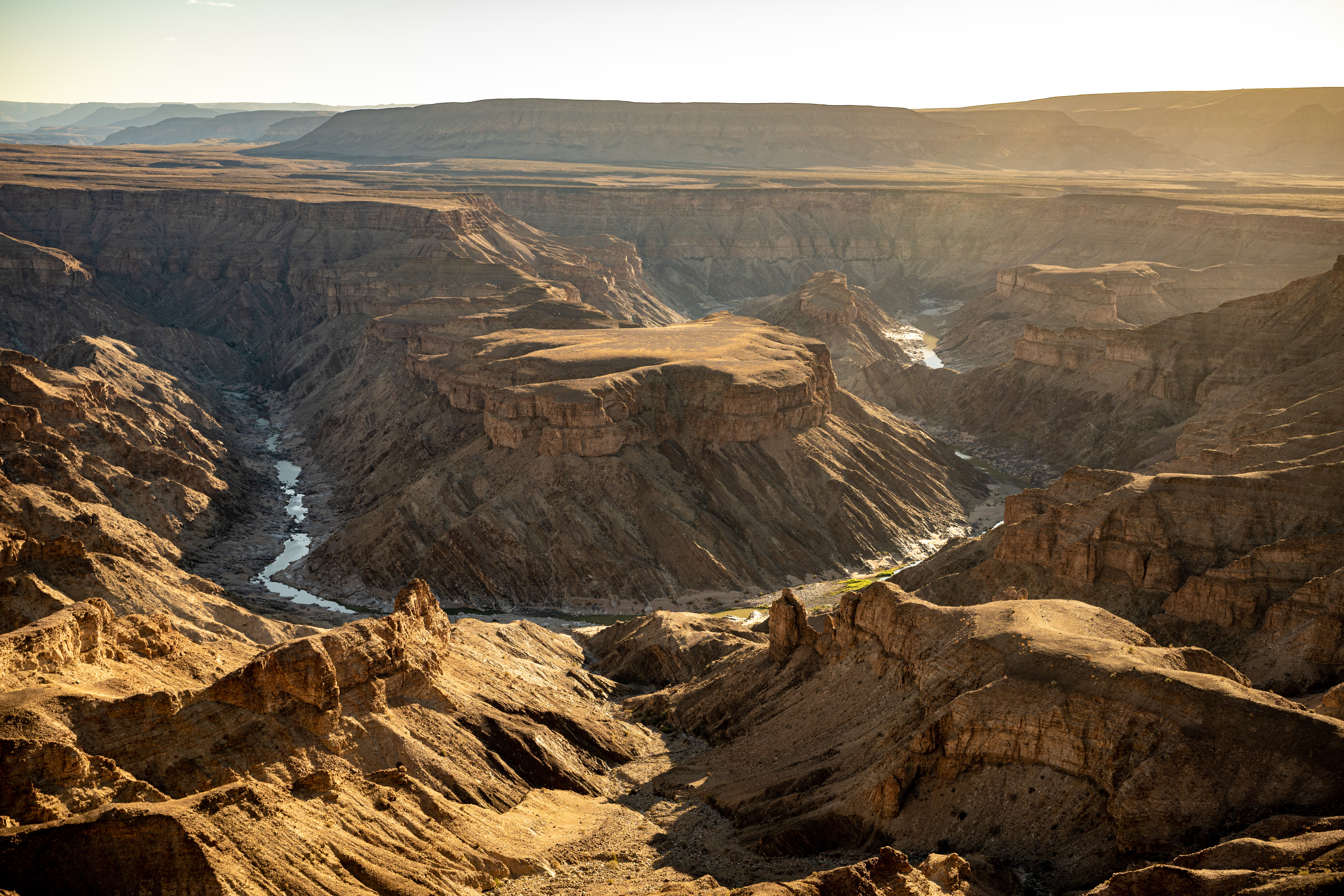 Aerial view of Fish River Canyon at sunset, layered rock walls and a river winding through the gorge floor