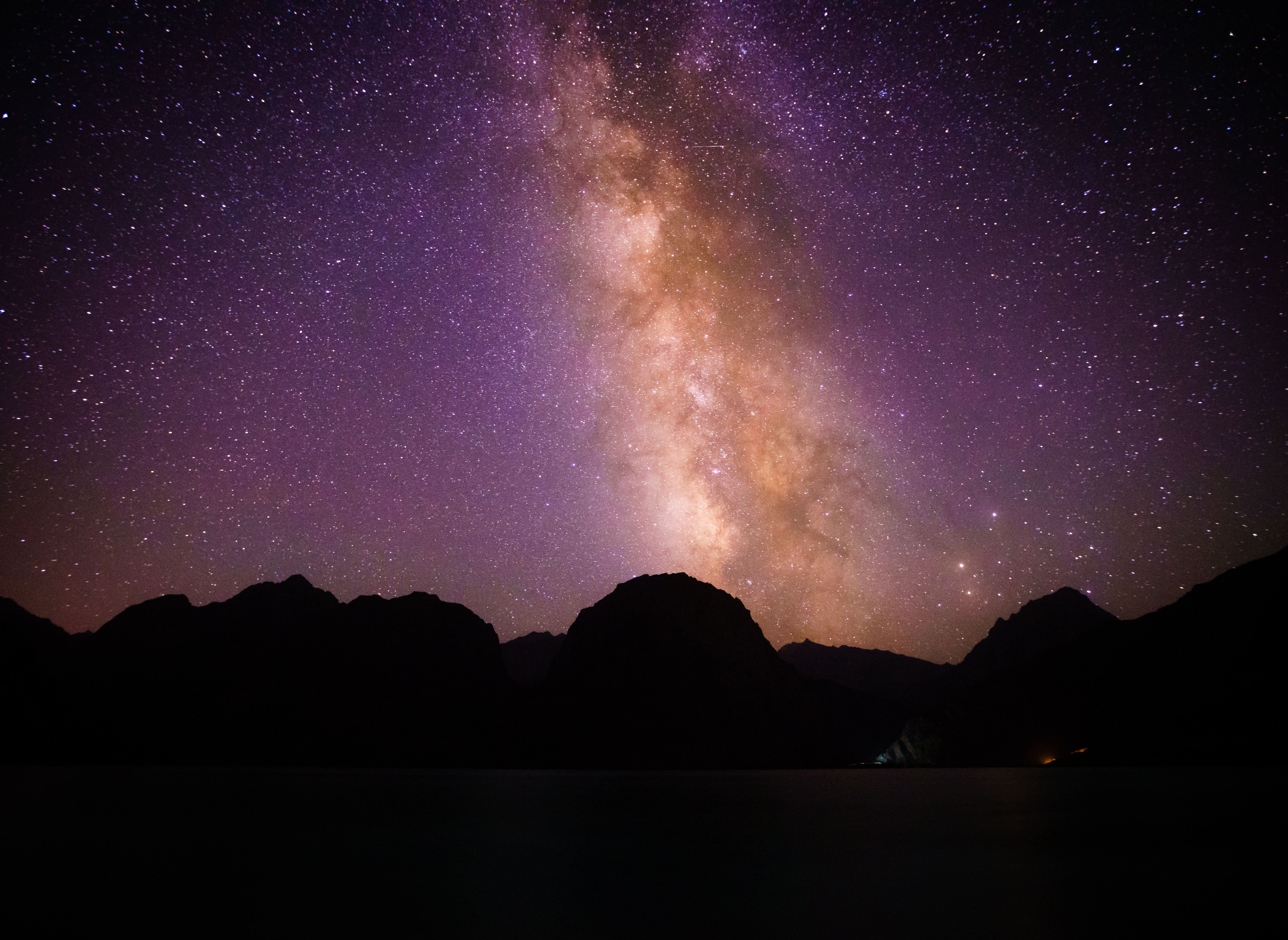 Milky Way arcing above dark mountain silhouettes surrounding Karakul Lake in Tajikistan, with stars filling the night sky